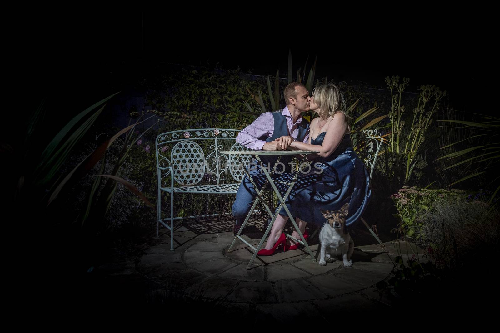 Quorn, UK - Aug 2019: Couple kissing on a garden bench at night, dog in forground