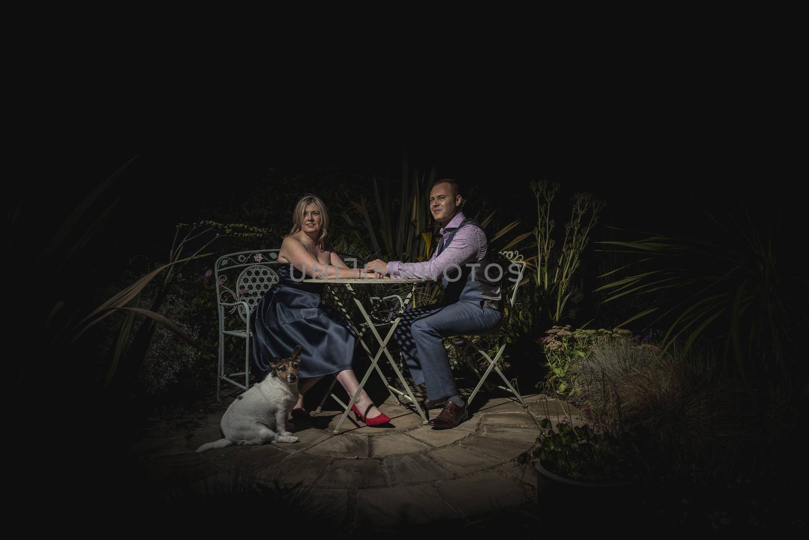 Quorn, UK - Aug 2019: Couple holding hands on a garden bench at night, dog in forground