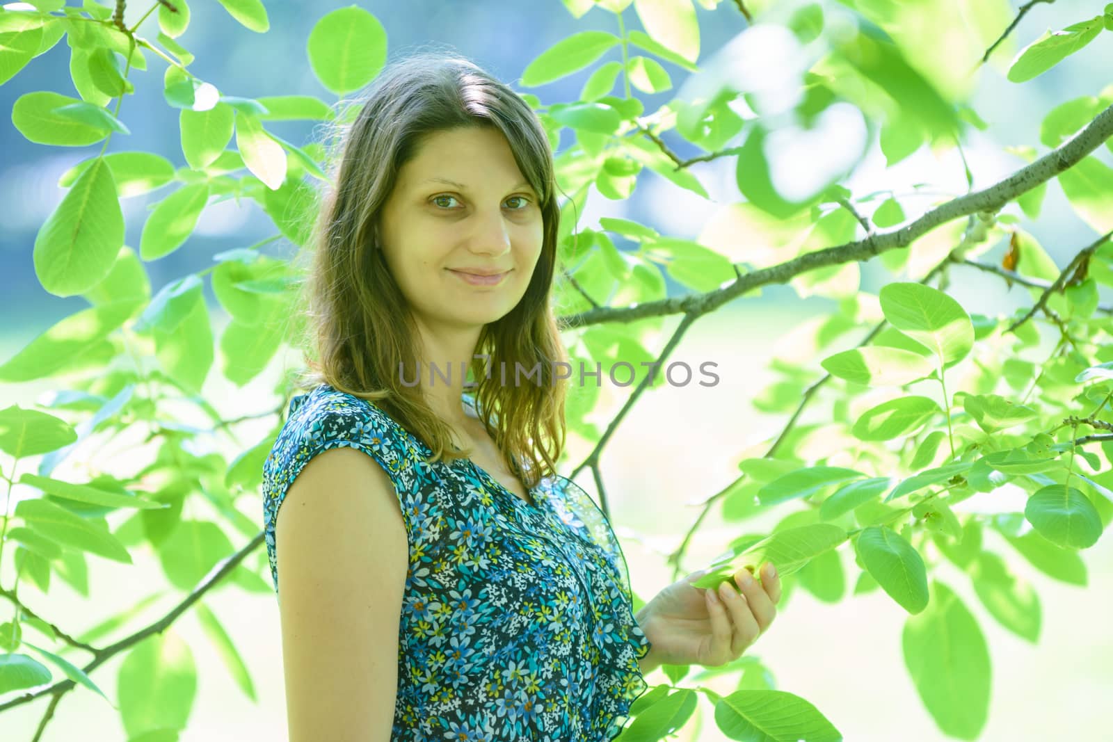 Girl smiles against a branch with green leaves in sunny weather