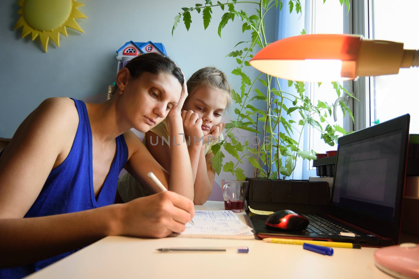 Mother solves daughter's assignments to study in notebooks at home at the desk by Madhourse