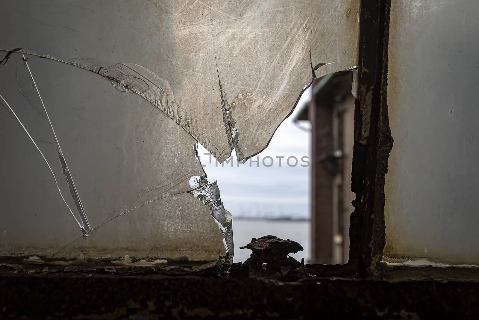 USA, New York, Ellis Island - May 2019: Small view of the beach though a broken glass pane in a rusty window casing