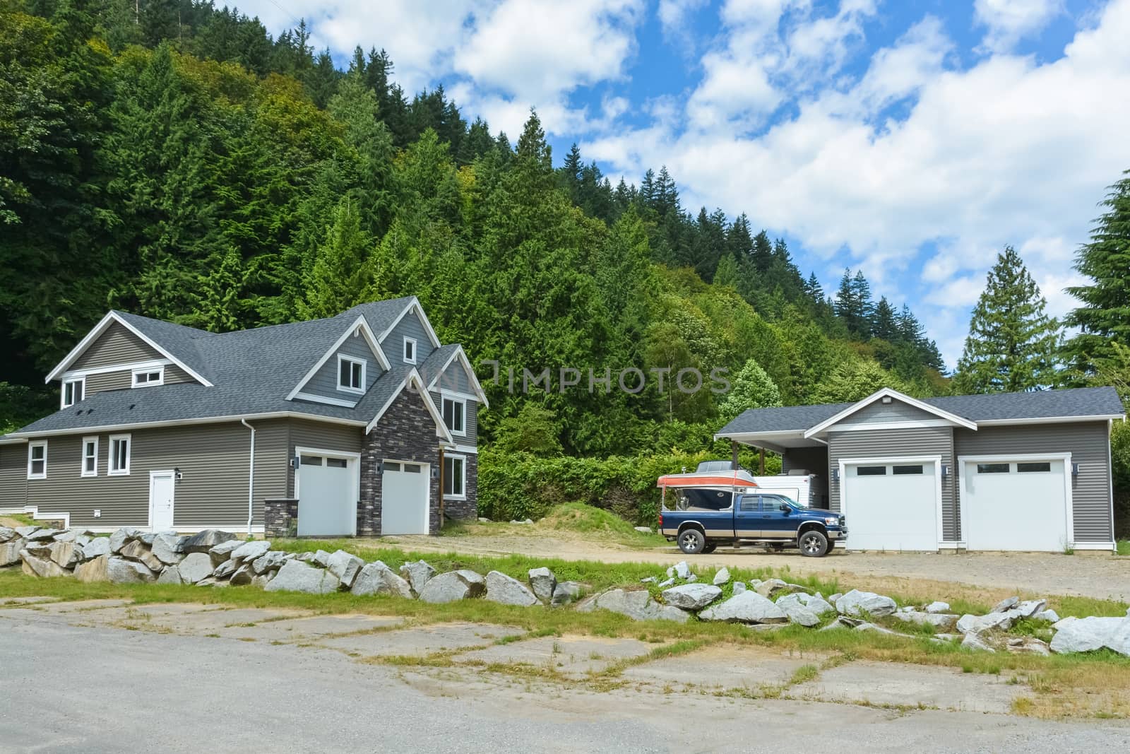 Brand new family house with car and boat parked on gravel driveway. New residential house and detached double garage on country side in British Columbia, Canada