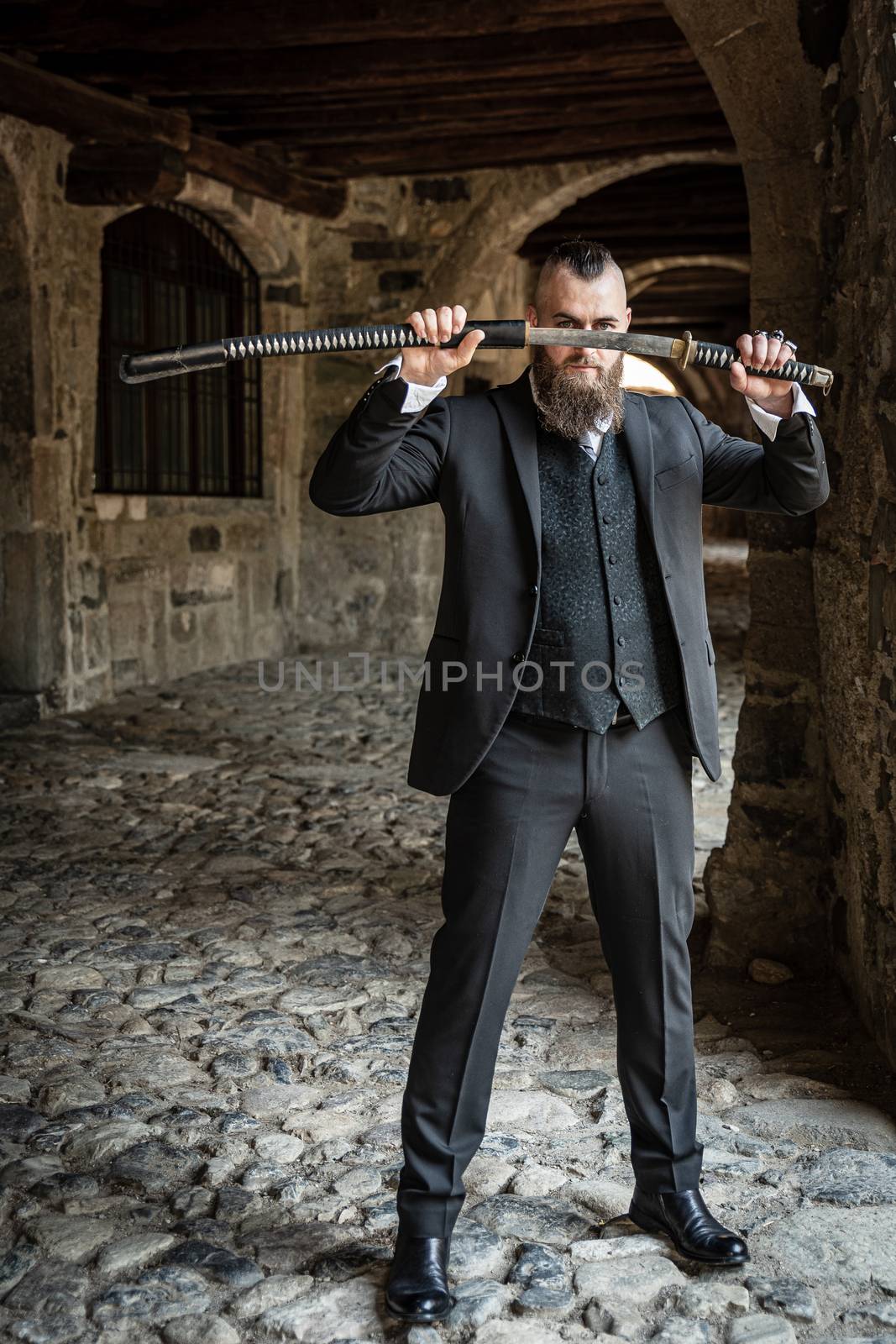 A man in elegant clothes shows off his katana at eye level, a young modern warrior in the alleys of a medieval town