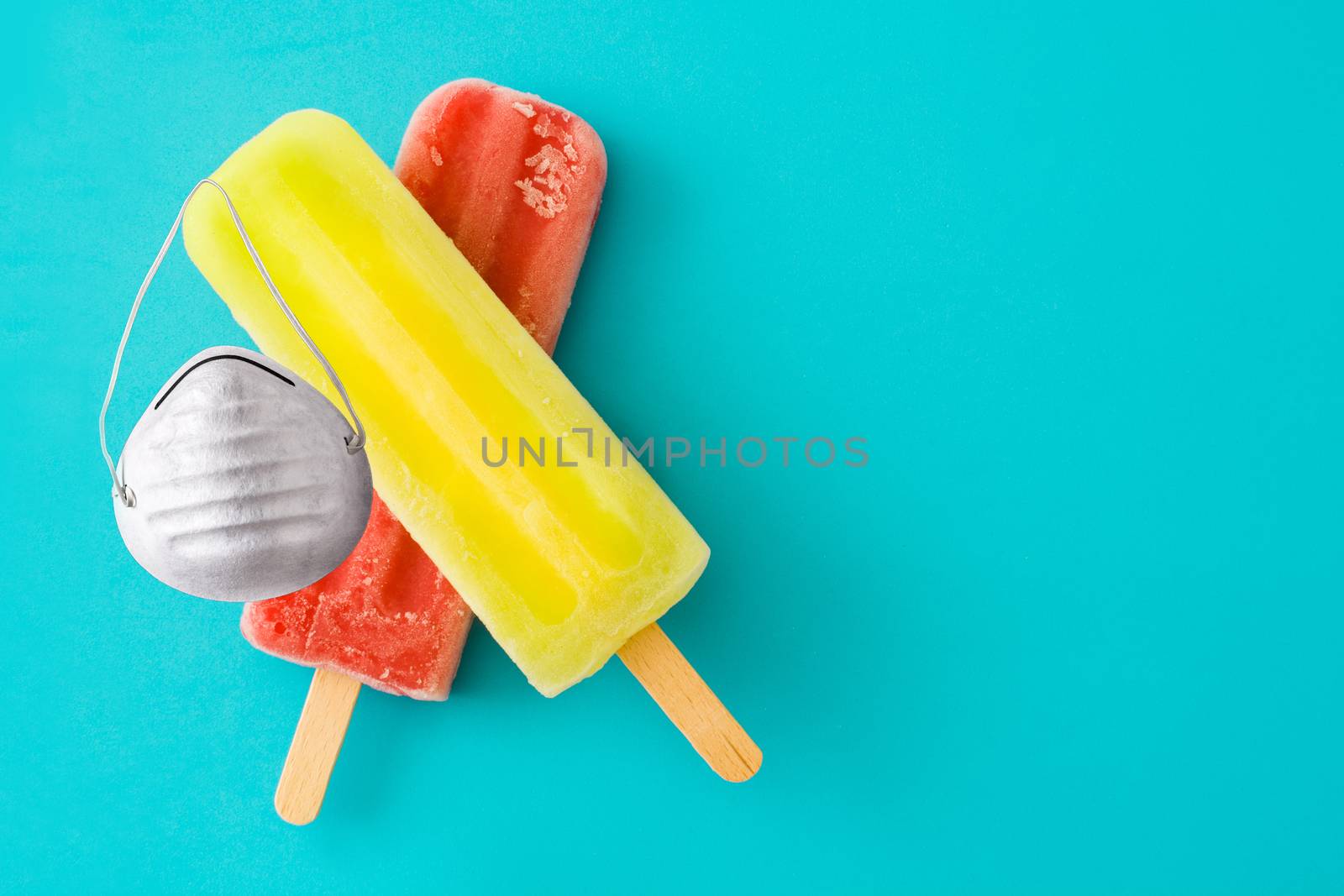 Lemon and strawberry popsicles with protective face mask on blue background