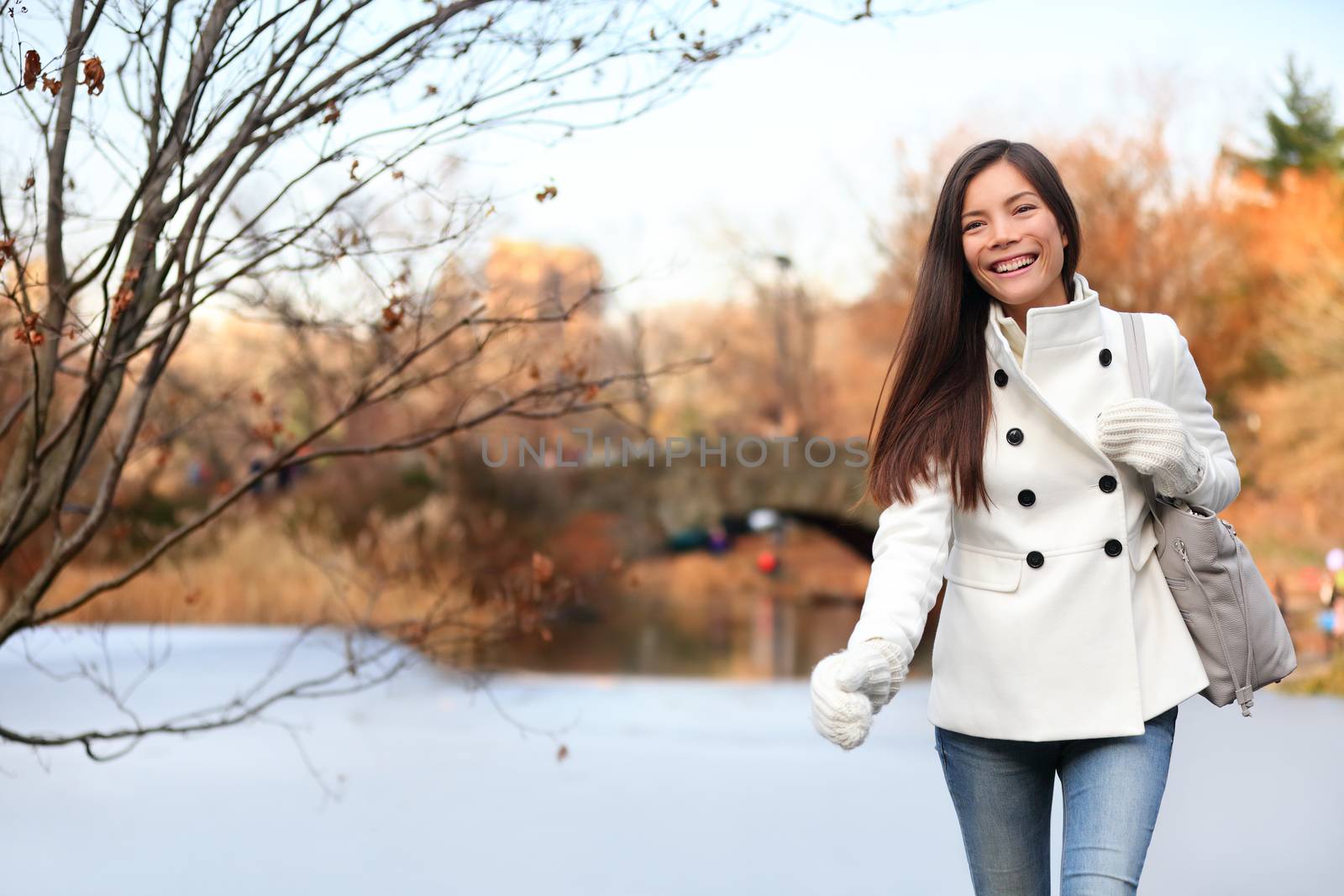 Woman walking happy in Central park, New York City in late fall early winter with skating rink in background. Candid smiling multi-ethnic girl on Manhattan, USA.