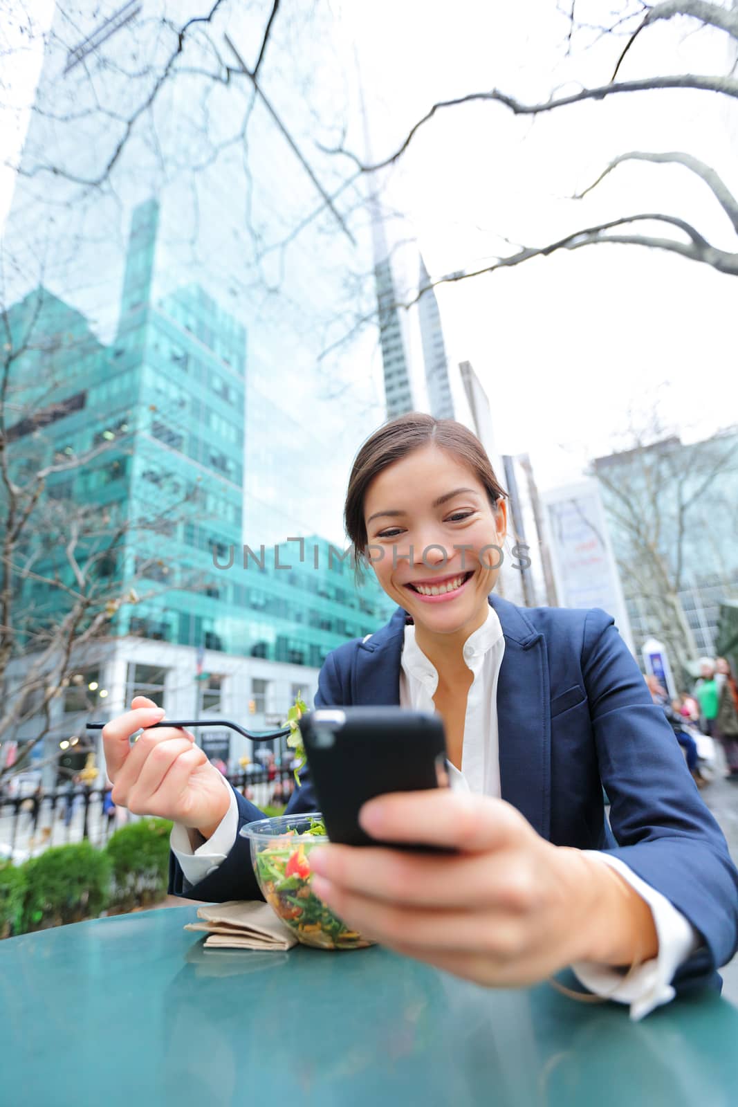 Young business woman on smartphone eating salad on lunch break in City Park living healthy lifestyle working on smart phone. Happy multiracial businesswoman, Bryant Park, manhattan, New York City, USA