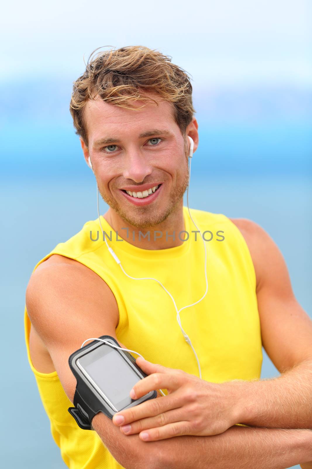 Running app on smartphone. Male runner listening to music adjusting settings on armband for smart phone. Fit man fitness model working outdoor by water.