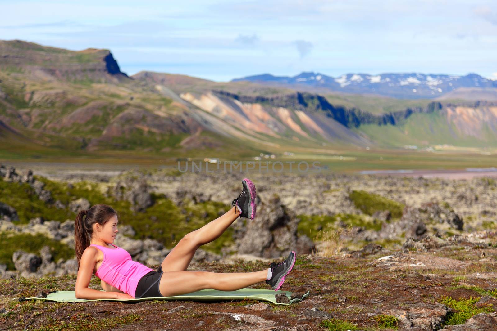 Fitness woman exercising in nature working on core strength doing scissor kick and flutter kicks exercise outdoor in amazing landscape on Iceland.