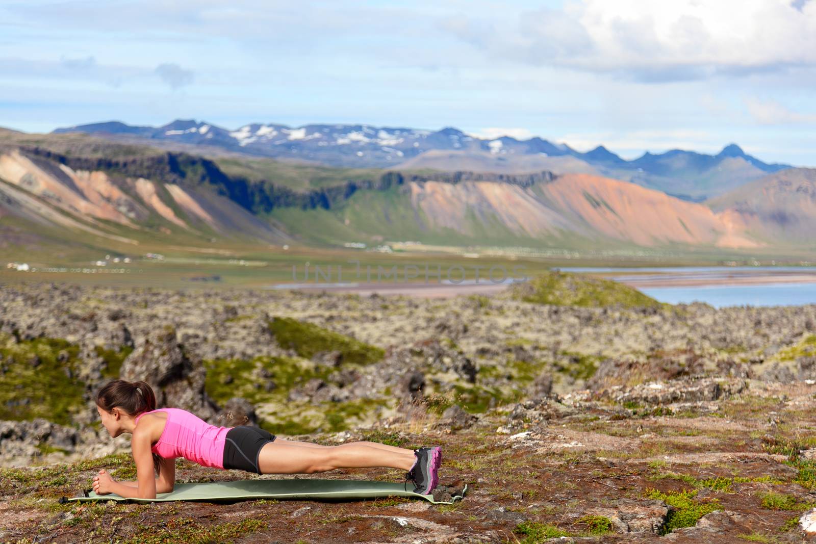 Exercising fitness woman doing plank in nature training core outside in amazing nature landscape on Iceland. Fit female sport model girl training outdoors. Mixed race Asian Caucasian athlete.