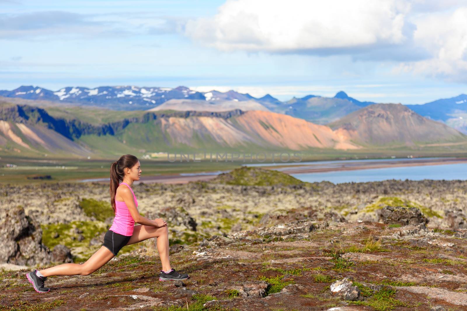 Fitness girl doing lunges exercise in nature. Female sport model exercising doing front forward lunge training legs and glute outside in beautiful landscape on Iceland.