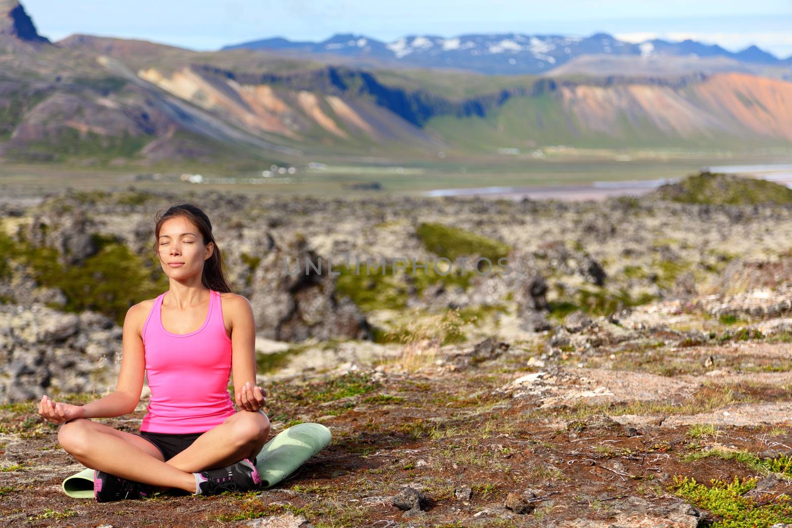Meditating yoga woman in meditation in nature. Female model relaxing in serene harmony in lotus position pose. Healthy wellness lifestyle image with multicultural young woman. Image from Iceland.