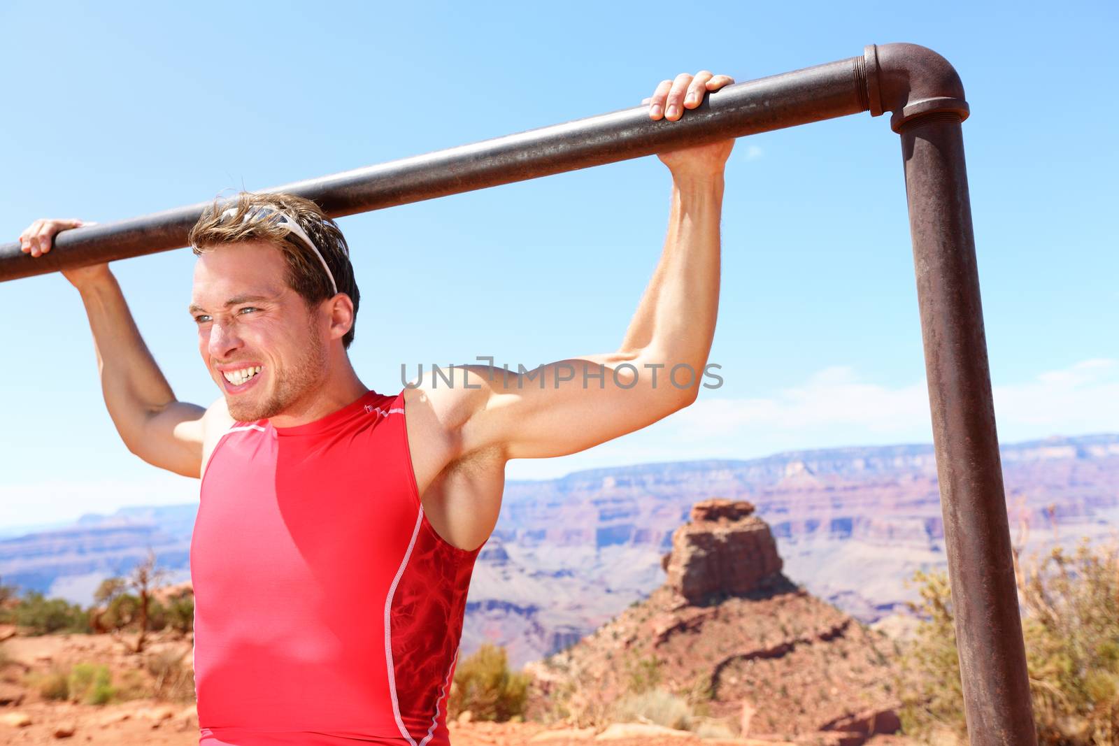 Exercising Fitness athlete man training pull ups in amazing nature landscape of Grand Canyon. Strength training fit male working out exercising outdoors in summer doing pull-ups and chin-ups.