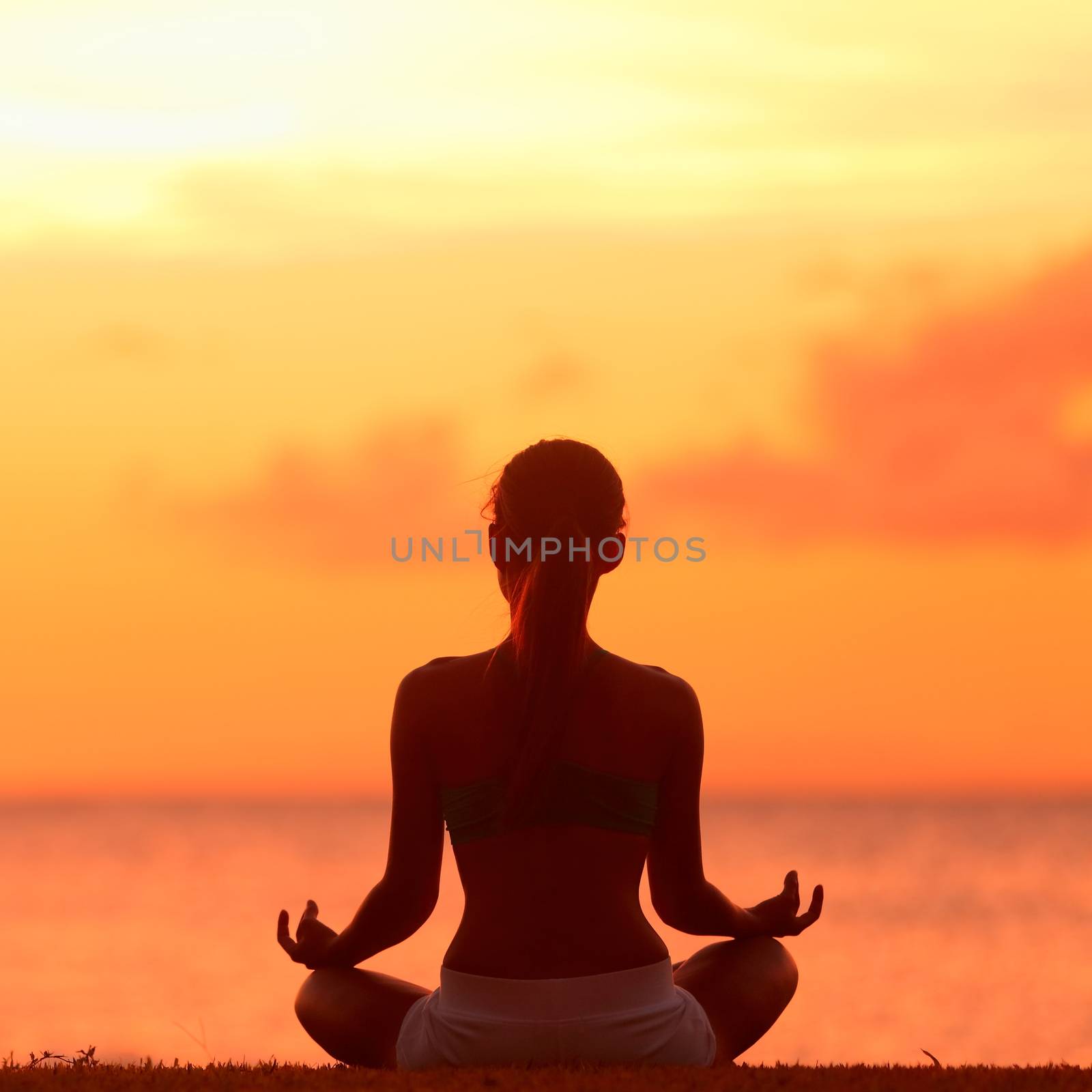 Meditation - Meditating yoga woman at at serene beach sunset. Girl relaxing in lotus pose in calm zen moment in the ocean water during yoga holidays resort retreat. Multiracial girl.