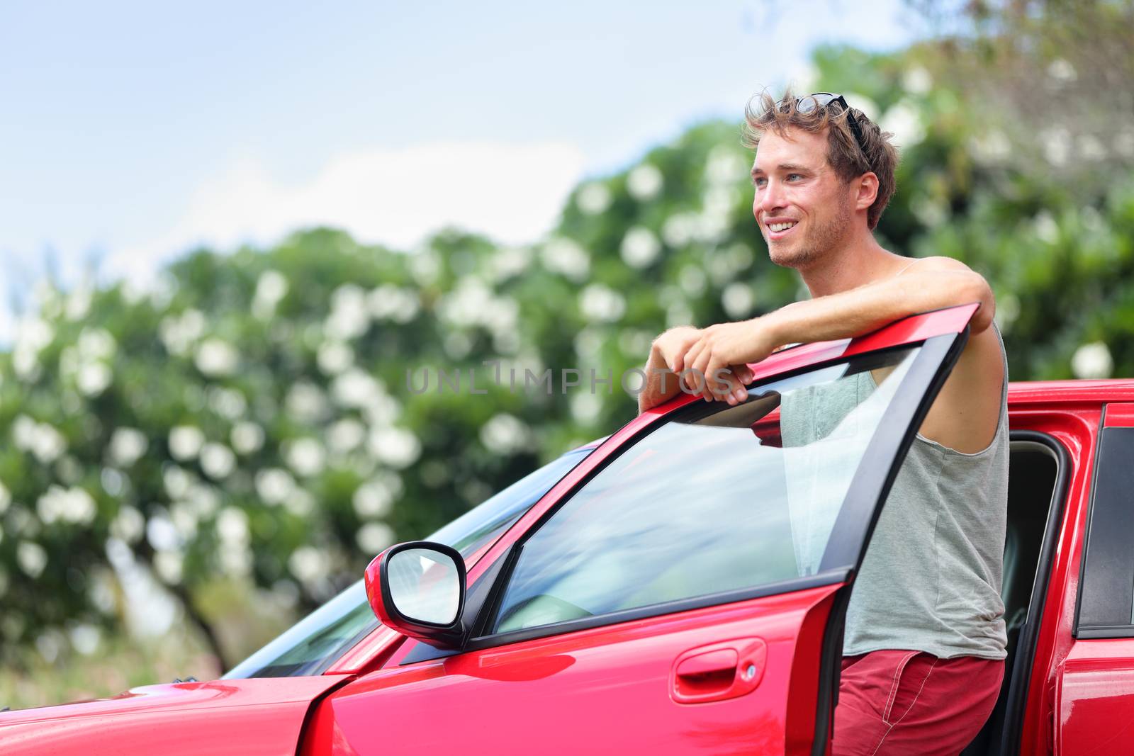 Car owner - young man and new red car outside. Happy male model leaning on door of a red sports car smiling.