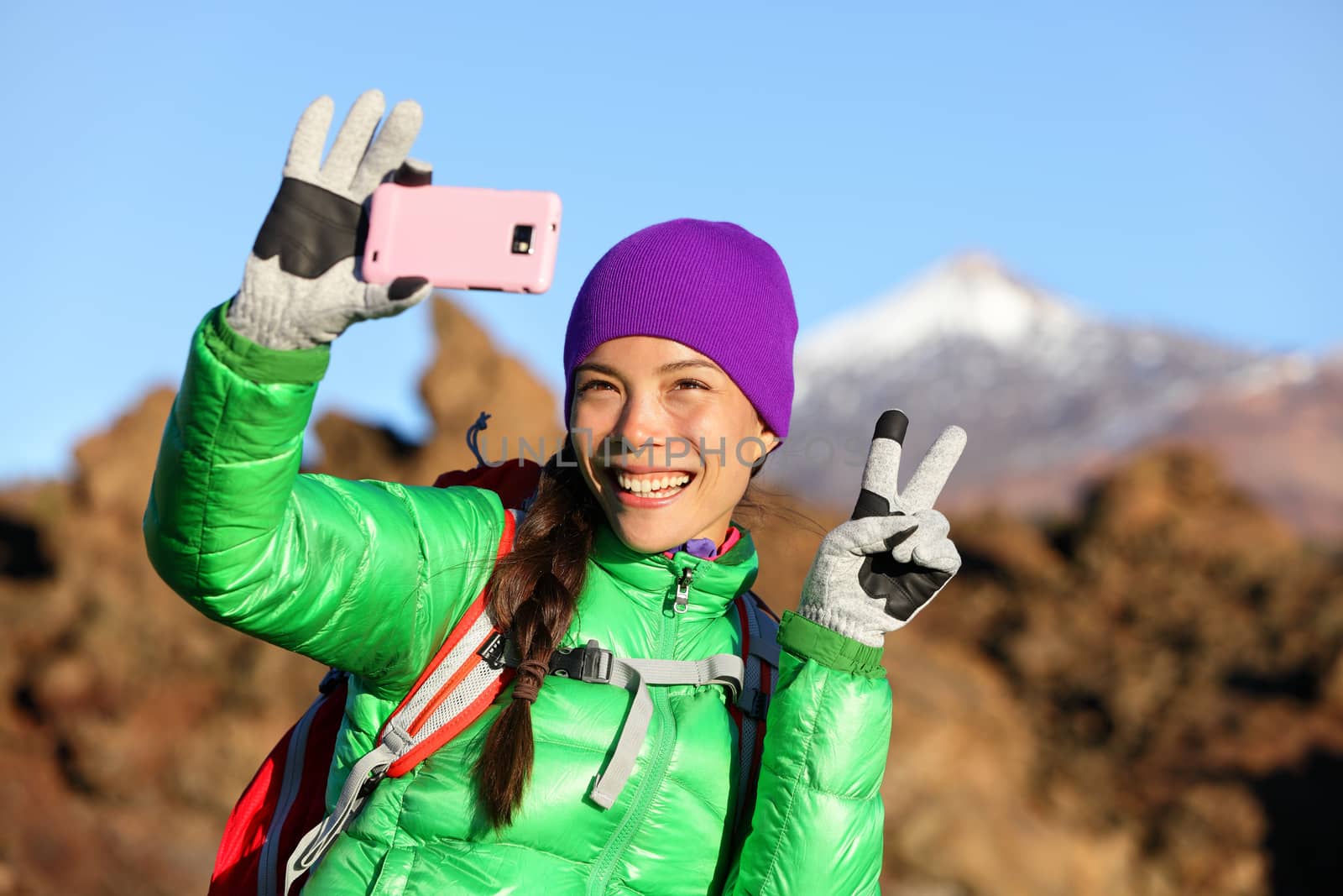 Woman hiker taking selfie photo using smartphone while hiking in winter jacket and clothing enjoying outdoor activity. Woman hiker taking self-portrait picture with smart phone camera.