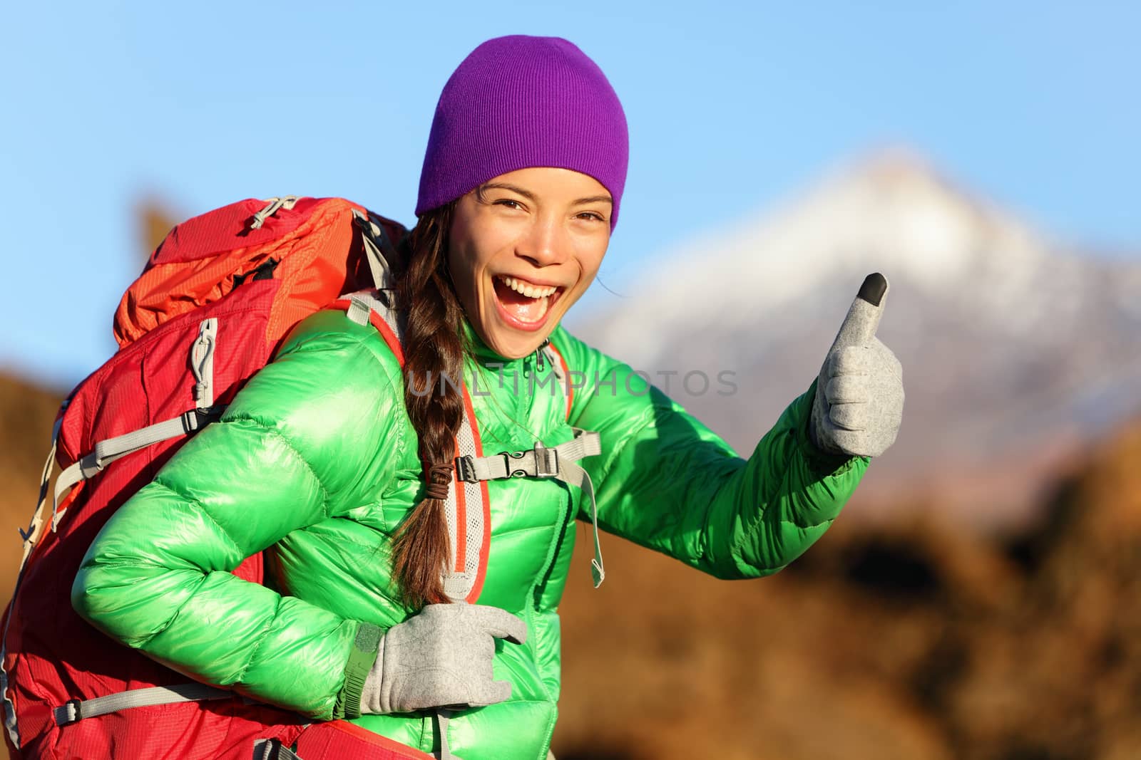 Hiking woman in winter jacket giving thumbs up smiling. Young Asian woman hiker smiling joyful at camera outdoor on hike trip. Beautiful young mixed race Asian Chinese / Caucasian woman in mountain.