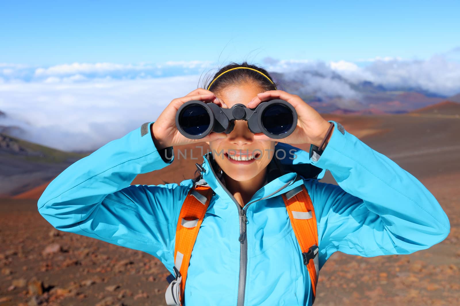 Hiker looking in binoculars enjoying spectacular view on mountain top above the clouds in Haleakala national park, Maui, Hawaii, USA.