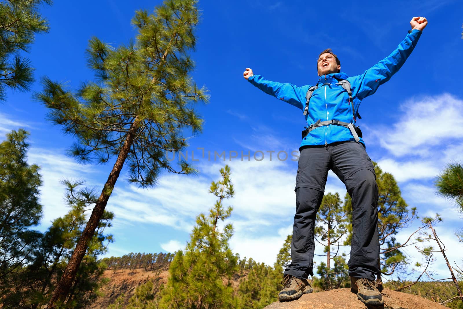 Man hiking reaching summit top cheering celebrating on mountain top with arms up outstretched towards the sky. Happy male hiker.