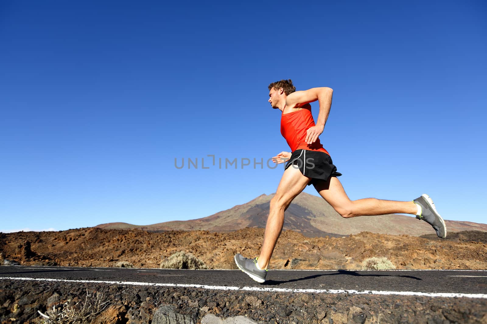 Sport running man - male runner training outdoors sprinting on mountain road in amazing landscape nature. Fit handsome jogger working out for marathon outside in summer.