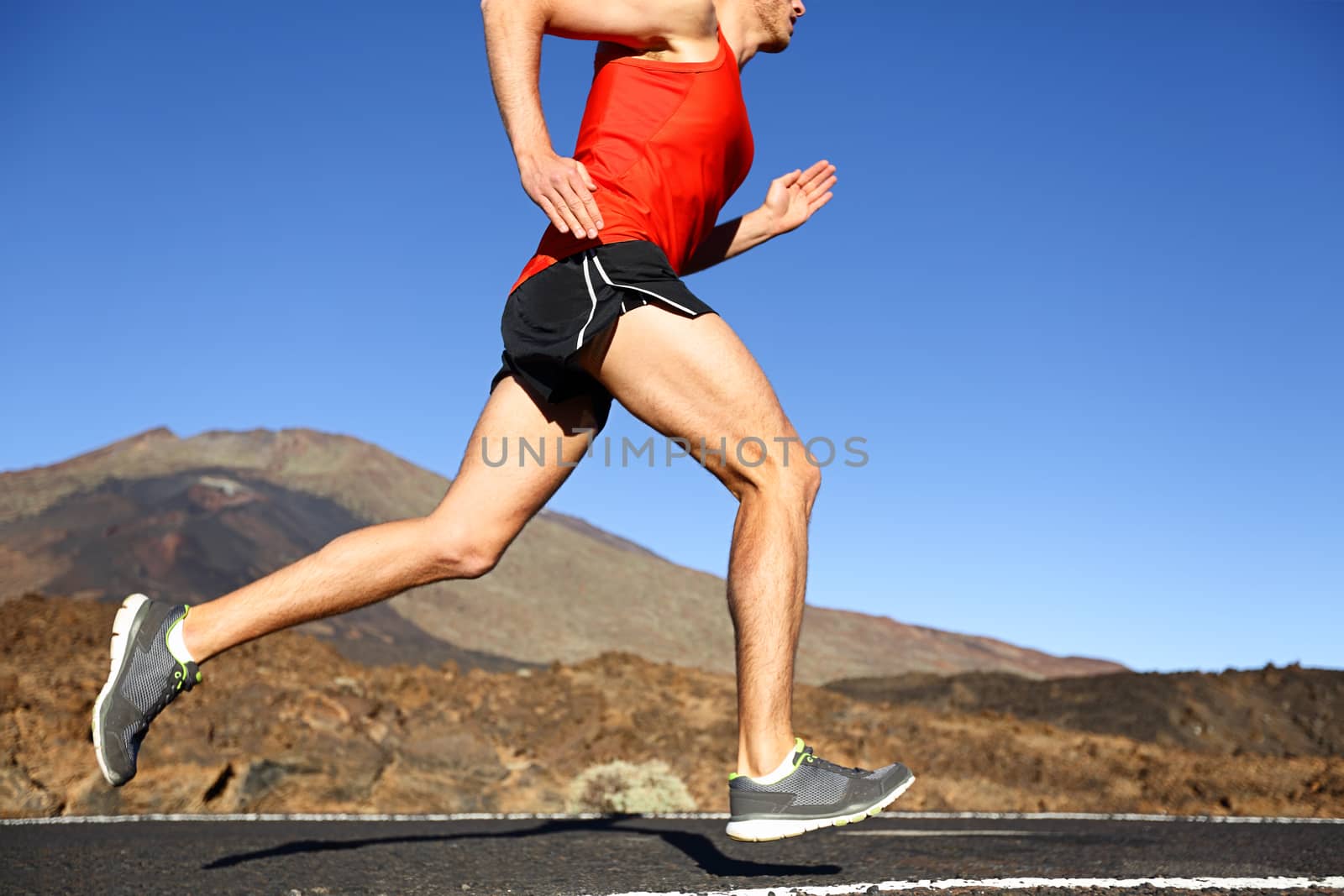 Running man - male runner training outdoors sprinting on mountain road in amazing landscape nature. Close up of fit handsome jogger working out for marathon outside in summer.