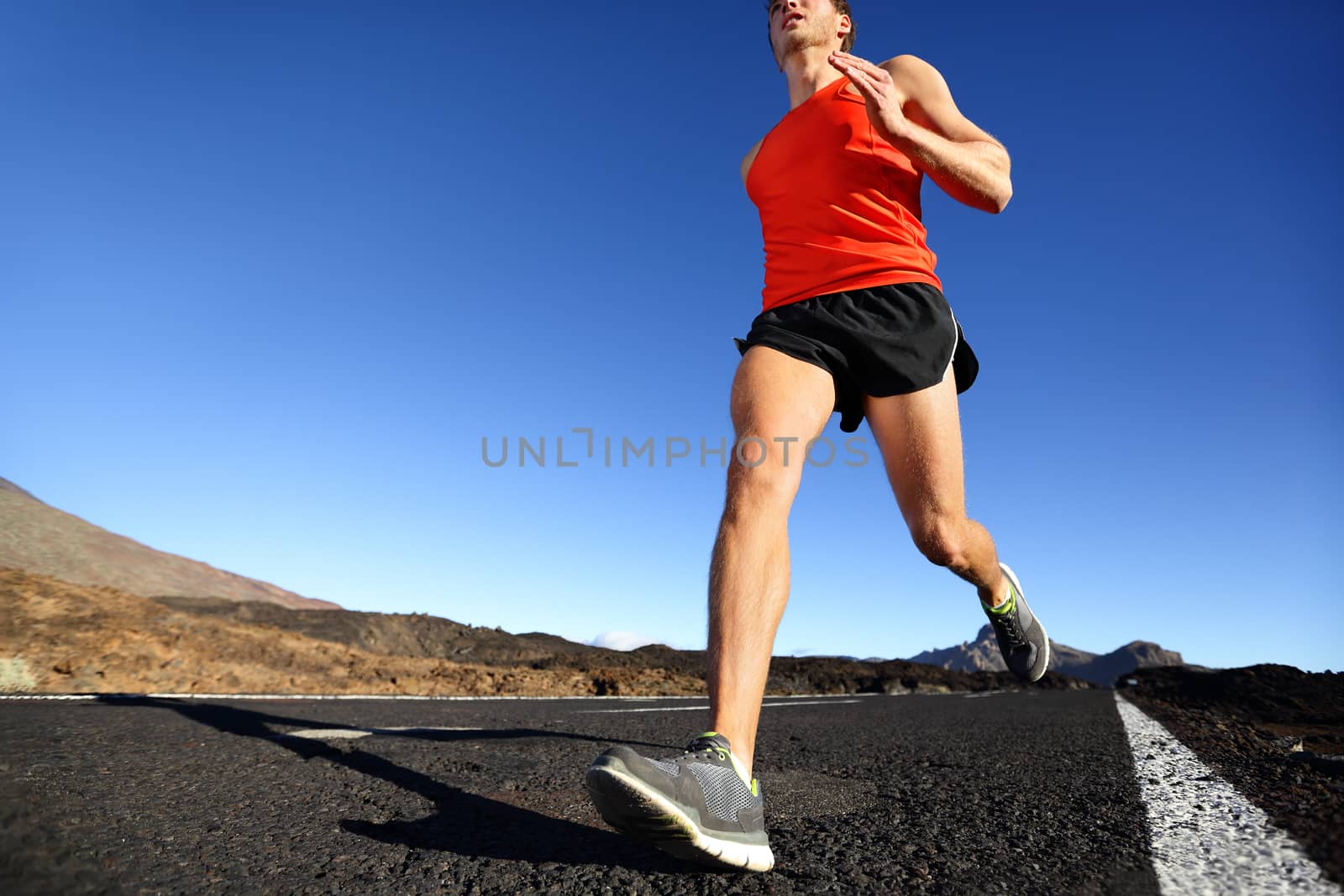 Sprinting running man - male runner training outdoors jogging on mountain road in amazing landscape nature. Close up of fit handsome jogger working out for marathon outside in summer.