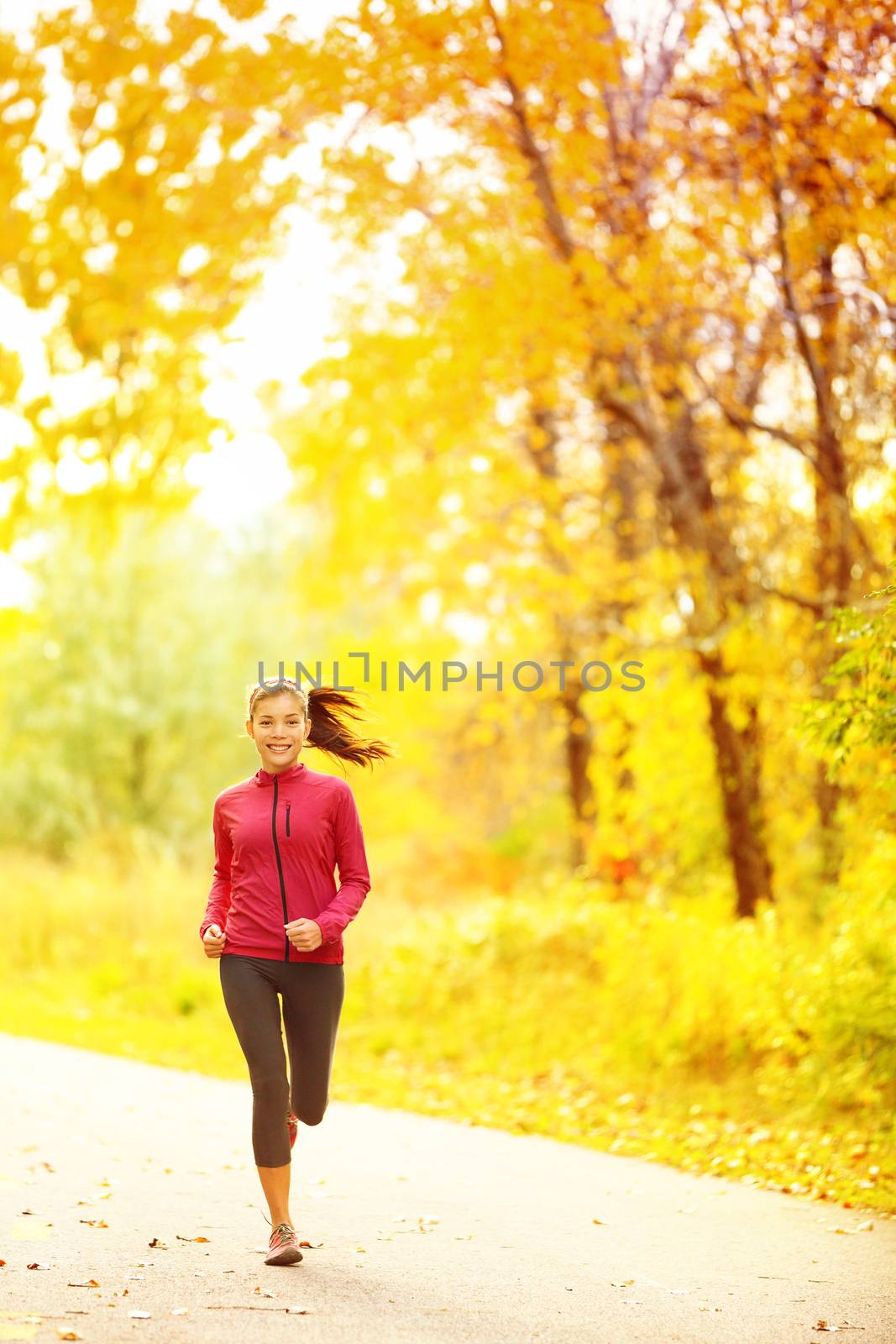Athlete runner woman running in fall autumn forest. Female fitness girl jogging on path in amazing fall foliage landscape nature outside.