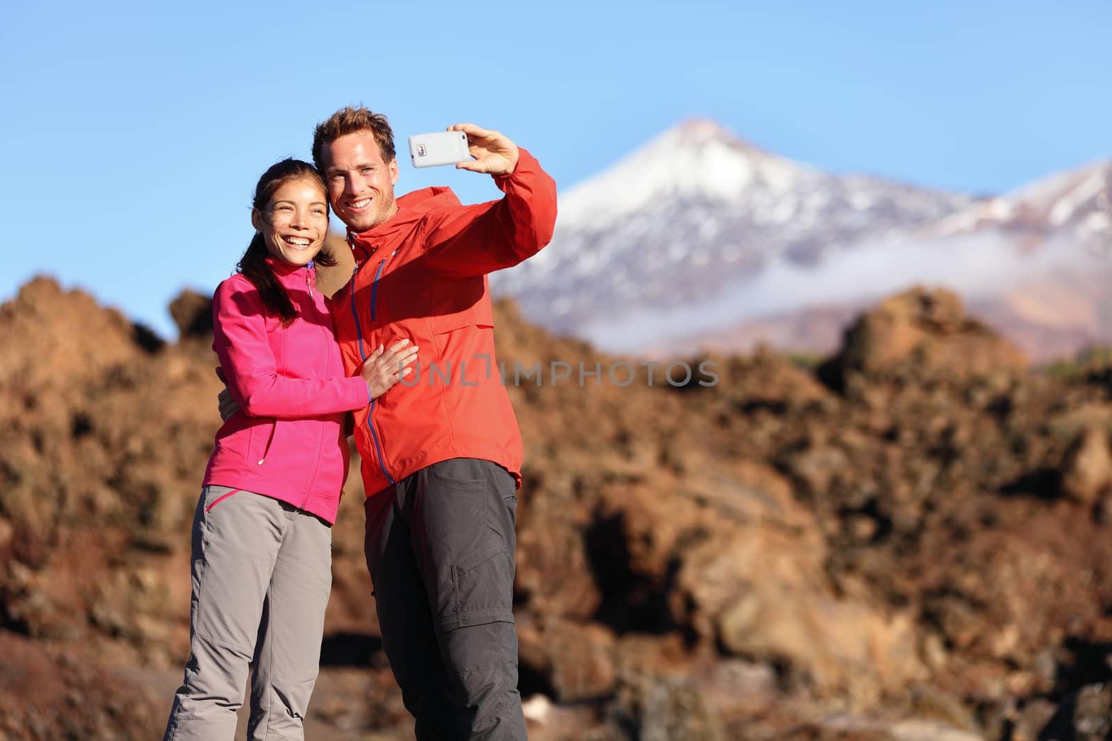 Couple taking selfie hiking in beautiful nature with smart phone. Happy couple walking enjoying view and taking pictures with smartphone. Man and woman by Volcano Teide on Tenerife, Canary Islands.