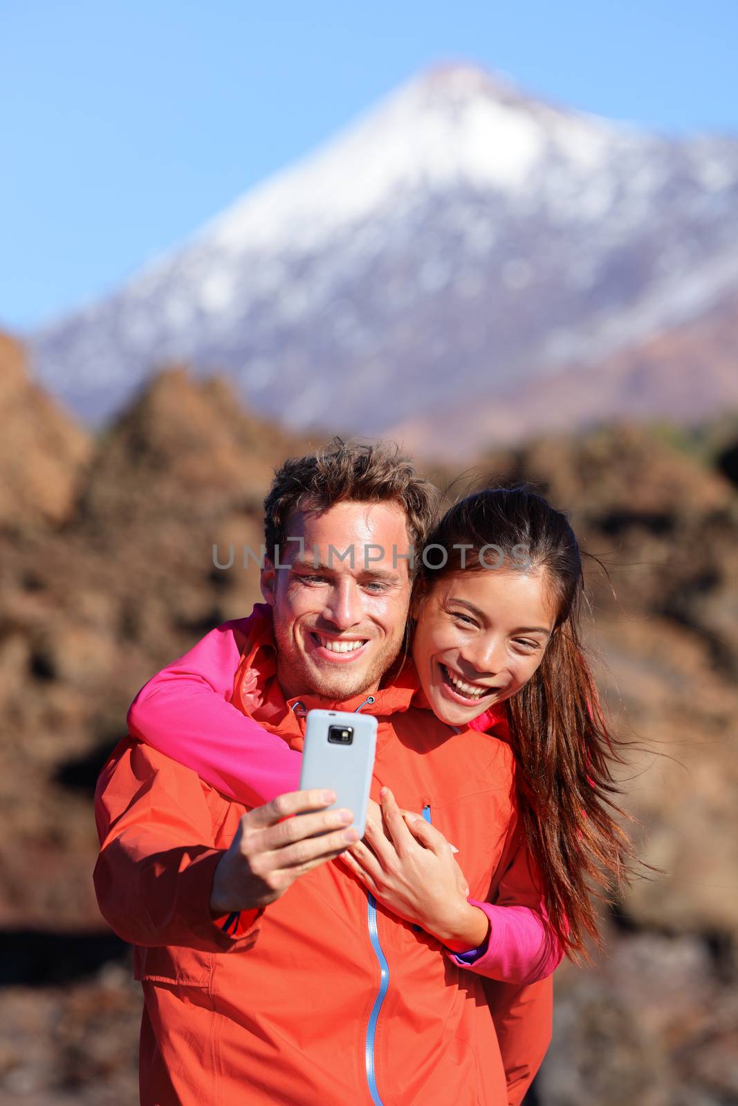 Selfie couple hiking in beautiful nature with smartphone. Happy couple walking enjoying view and taking pictures with smart phone. Man and woman by Volcano Teide on Tenerife, Canary Islands.