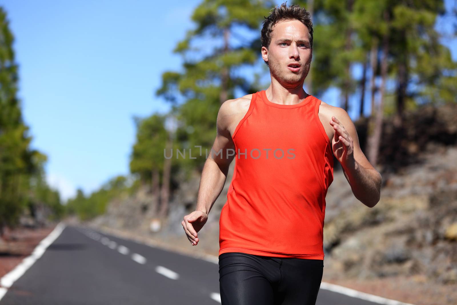 Sprinting runner man running at fast speed. Male sport sprinter training hard. Young strong male fitness model during run outdoors in beautiful landscape.