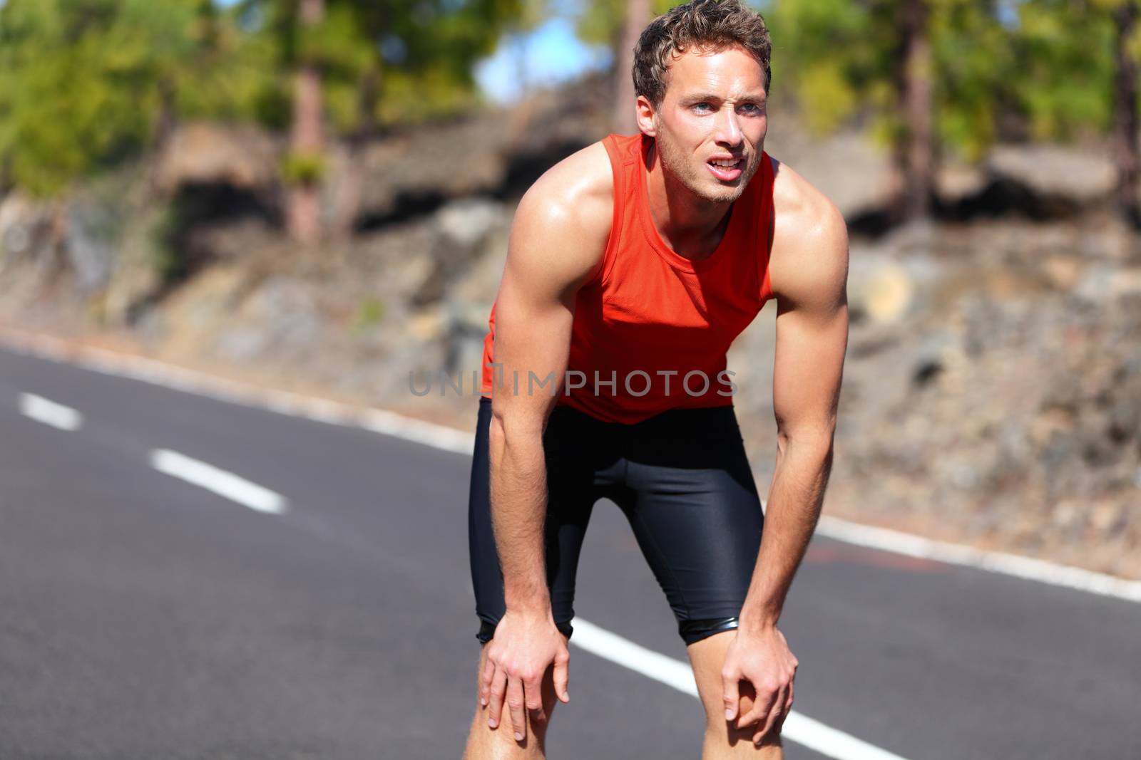 Runner resting after running. Jogging man taking a break during training outdoors in on mountain road. Young Caucasian male fitness model after work out.