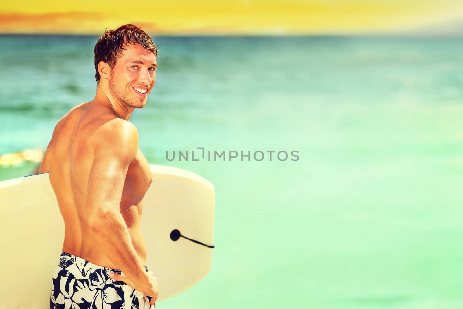 Surfer man going surfing on summer beach. Male bodyboarding surfing man good looking standing with bodyboard surfboard during vacation holidays getaway. Caucasian water sport model in his 20s.