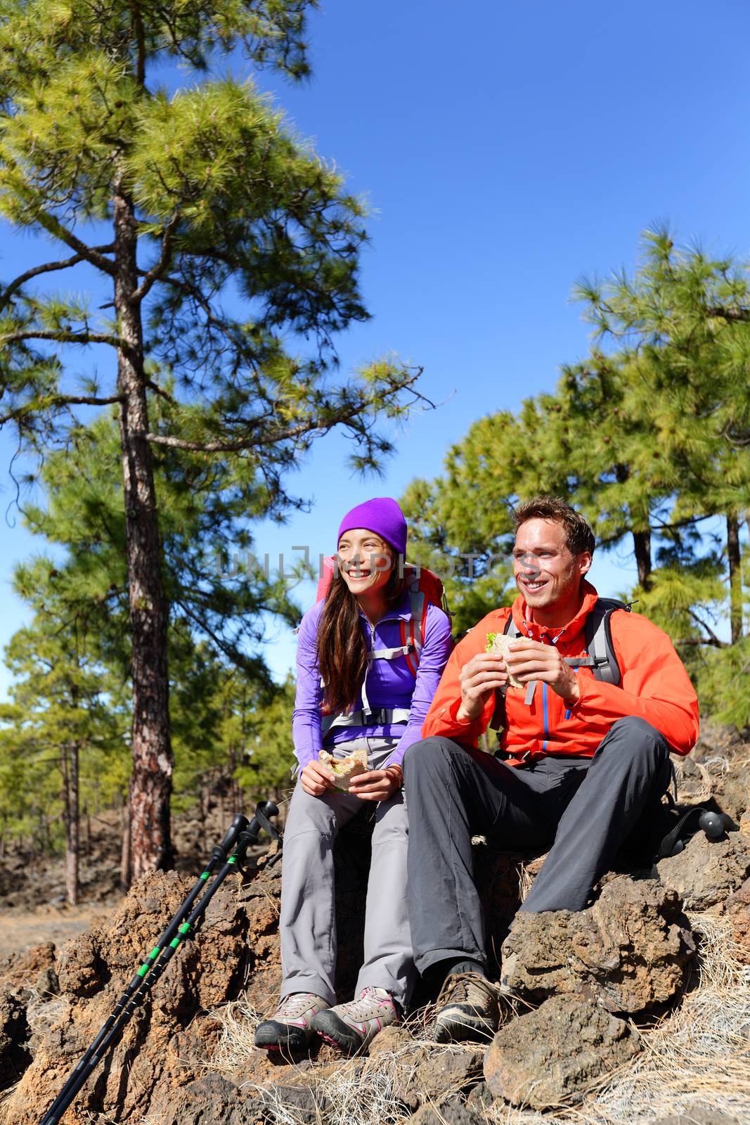 Hikers couple relaxing eating lunch sandwich. Hiking people living active lifestyle in mountain nature. Woman and man hiker sitting during hike on volcano Teide, Tenerife, Canary Islands, Spain.