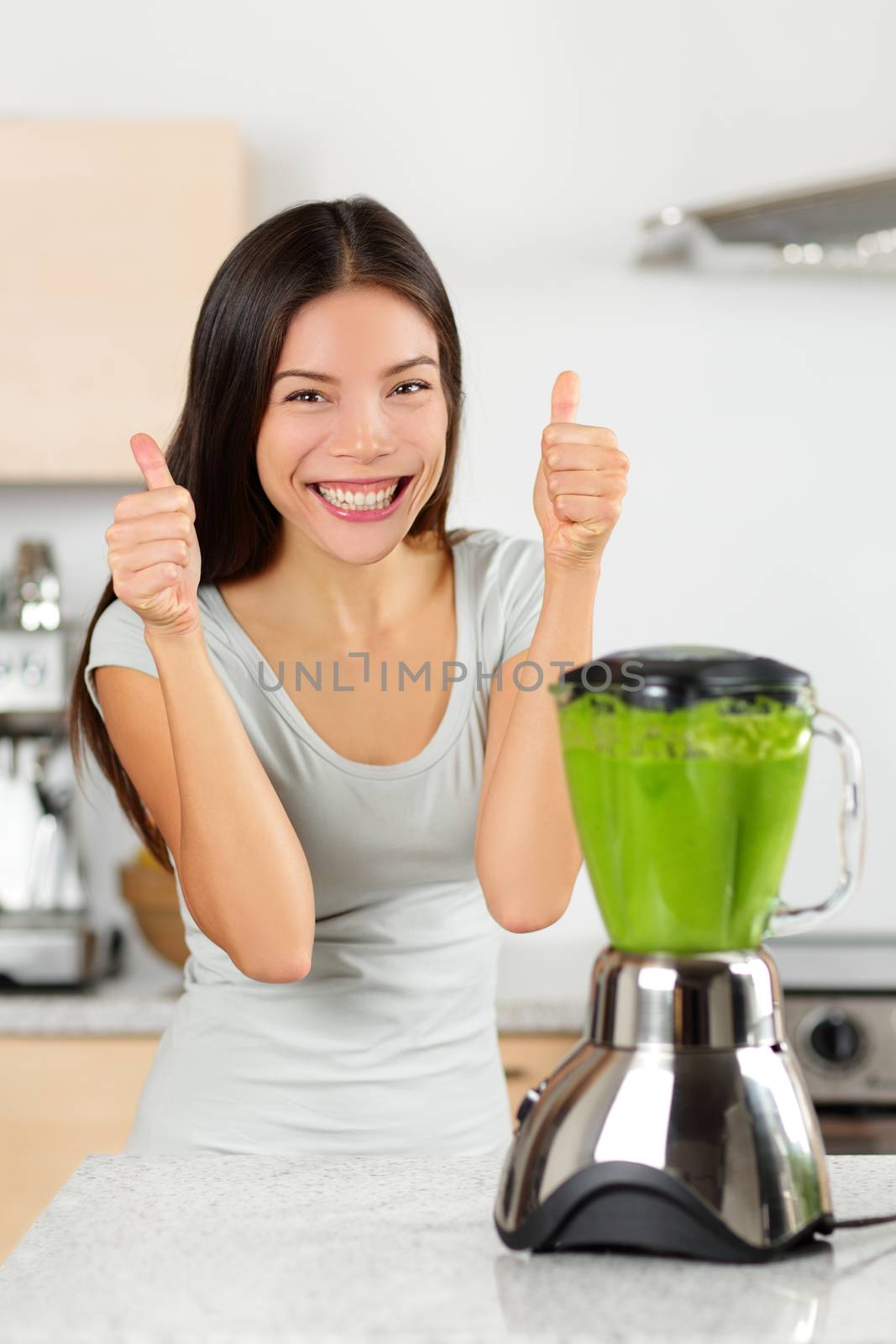 Vegetable smoothie woman happy thumbs up blending green smoothies with blender home in kitchen. Healthy eating lifestyle concept portrait of beautiful young woman preparing drink with spinach, carrots, celery etc.