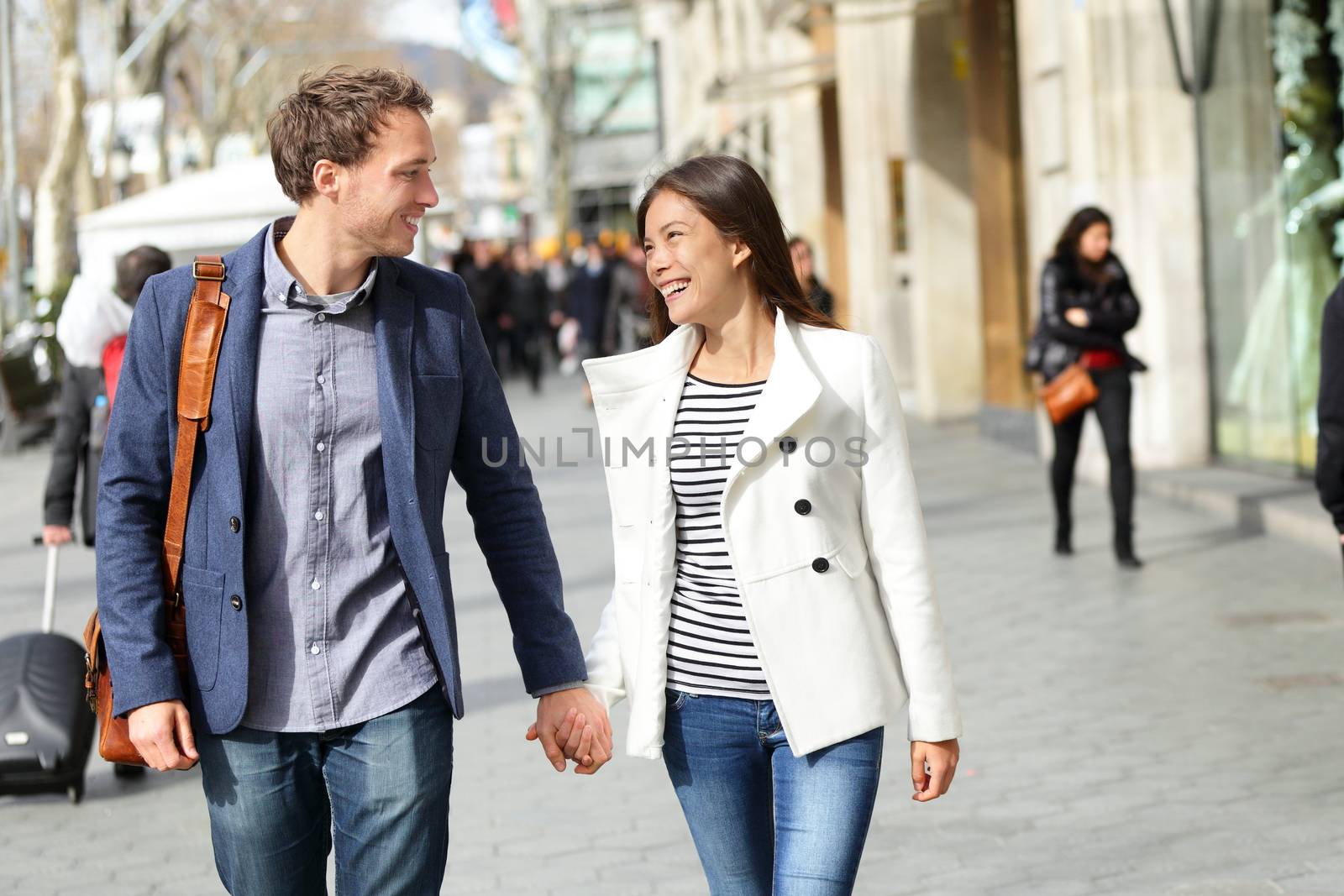 Urban modern professionals couple walking romantic laughing talking holding hands on date. Young multicultural couple Asian and Caucasian. From famous Passeig de Gracia, Barcelona, Catalonia, Spain.