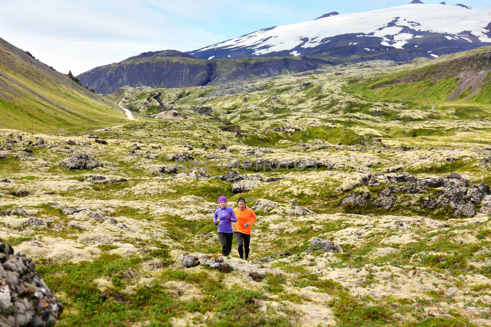 Running sport. Runners on cross country trail run outdoors working out for marathon. Fit young fitness model man and asian woman training together outside in mountain nature on Snaefellsnes, Iceland.