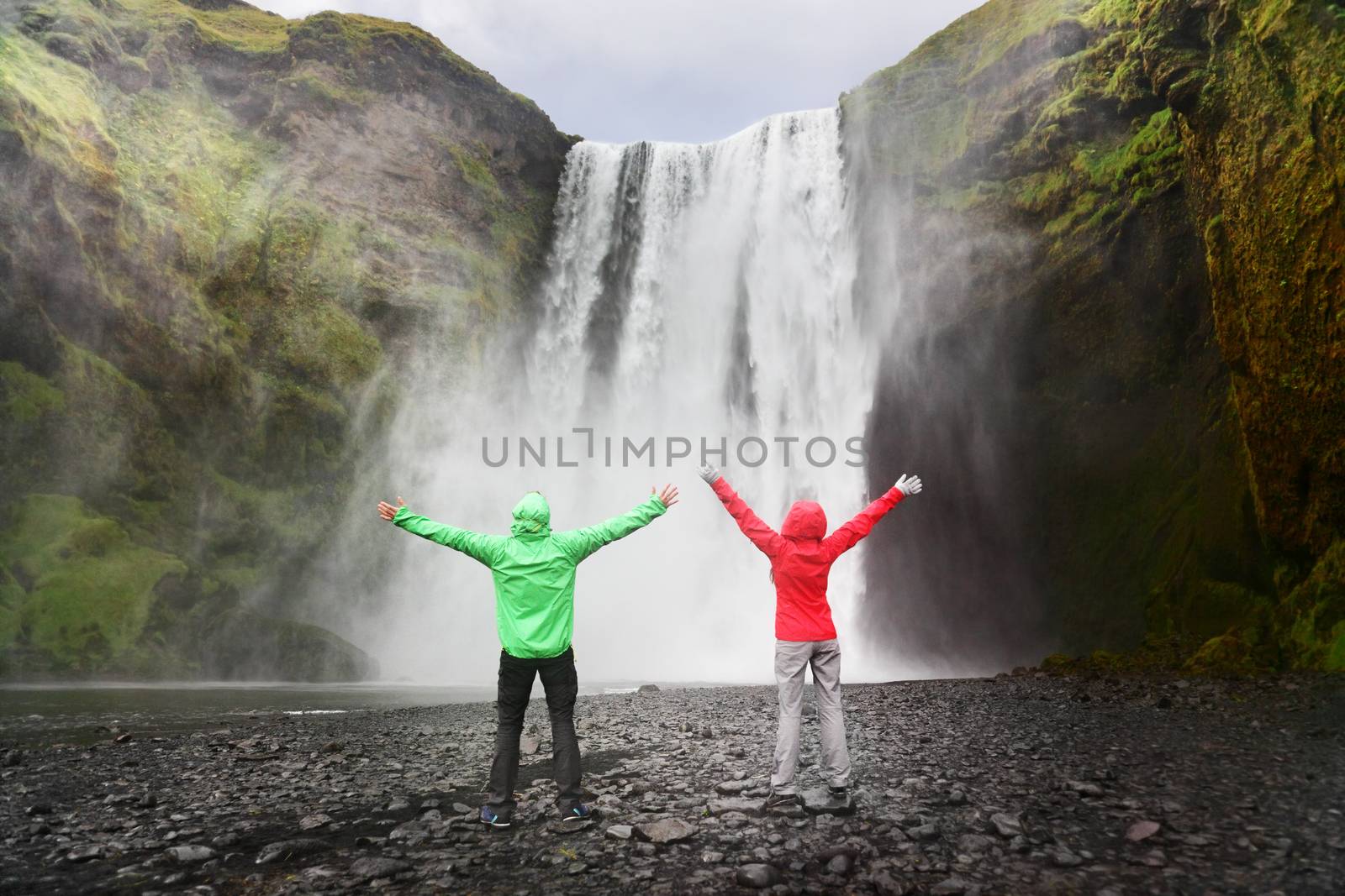 People by Skogafoss waterfall on Iceland golden circle. Couple visiting famous tourist attractions and landmarks in Icelandic nature landscape.