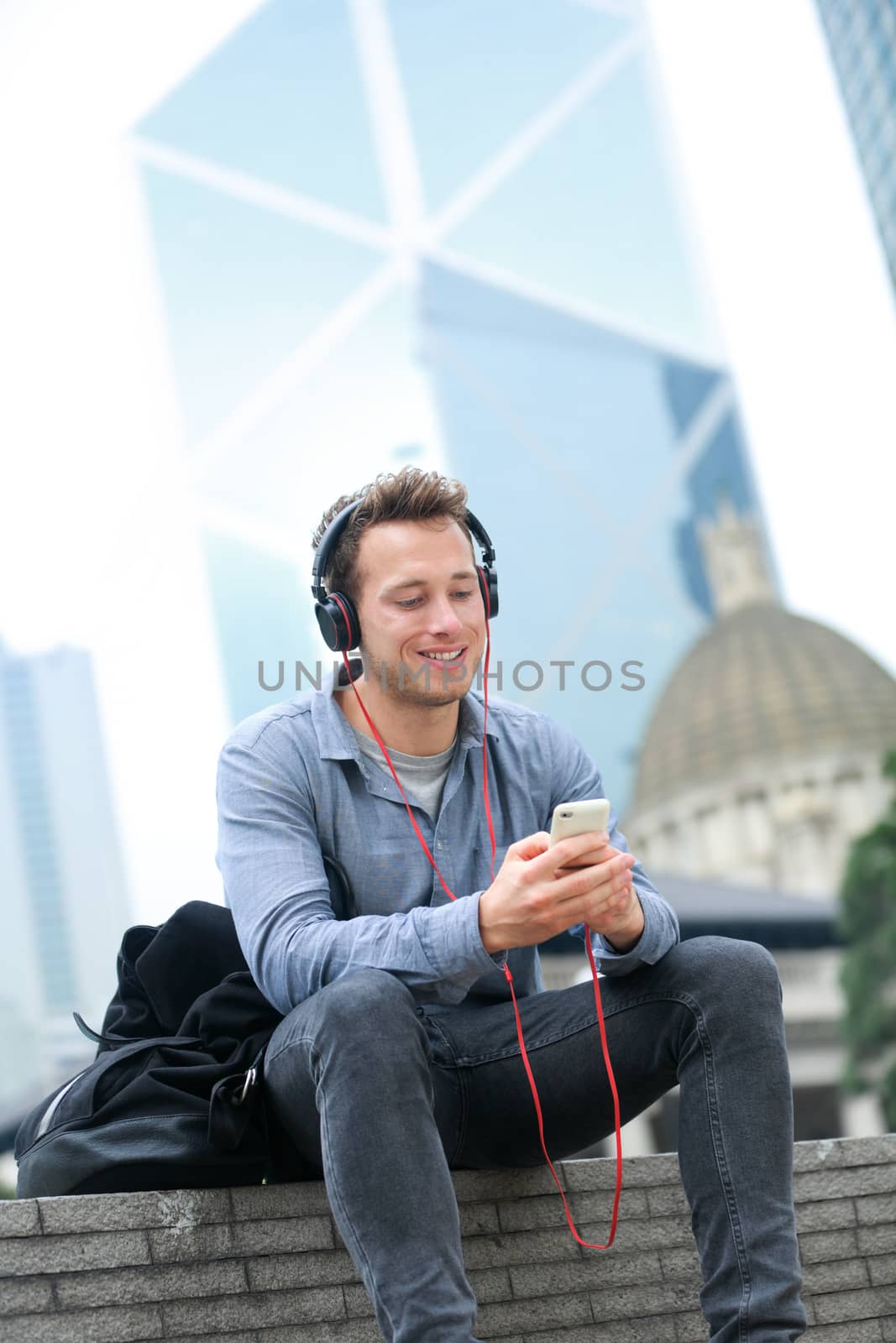 Urban man on smart phone wearing headphones listening to music or having video chat conversation sitting outside using app on 4g smartphones. Casual young urban professional male in Hong Kong Central.