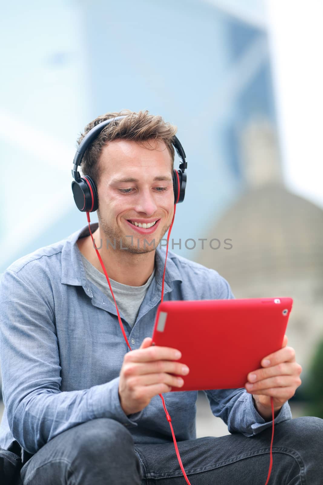 Video chat conversation. Man talking on tablet pc sitting outside using app on 4g wireless device wearing headphones. Casual young urban professional male in his late 20s.