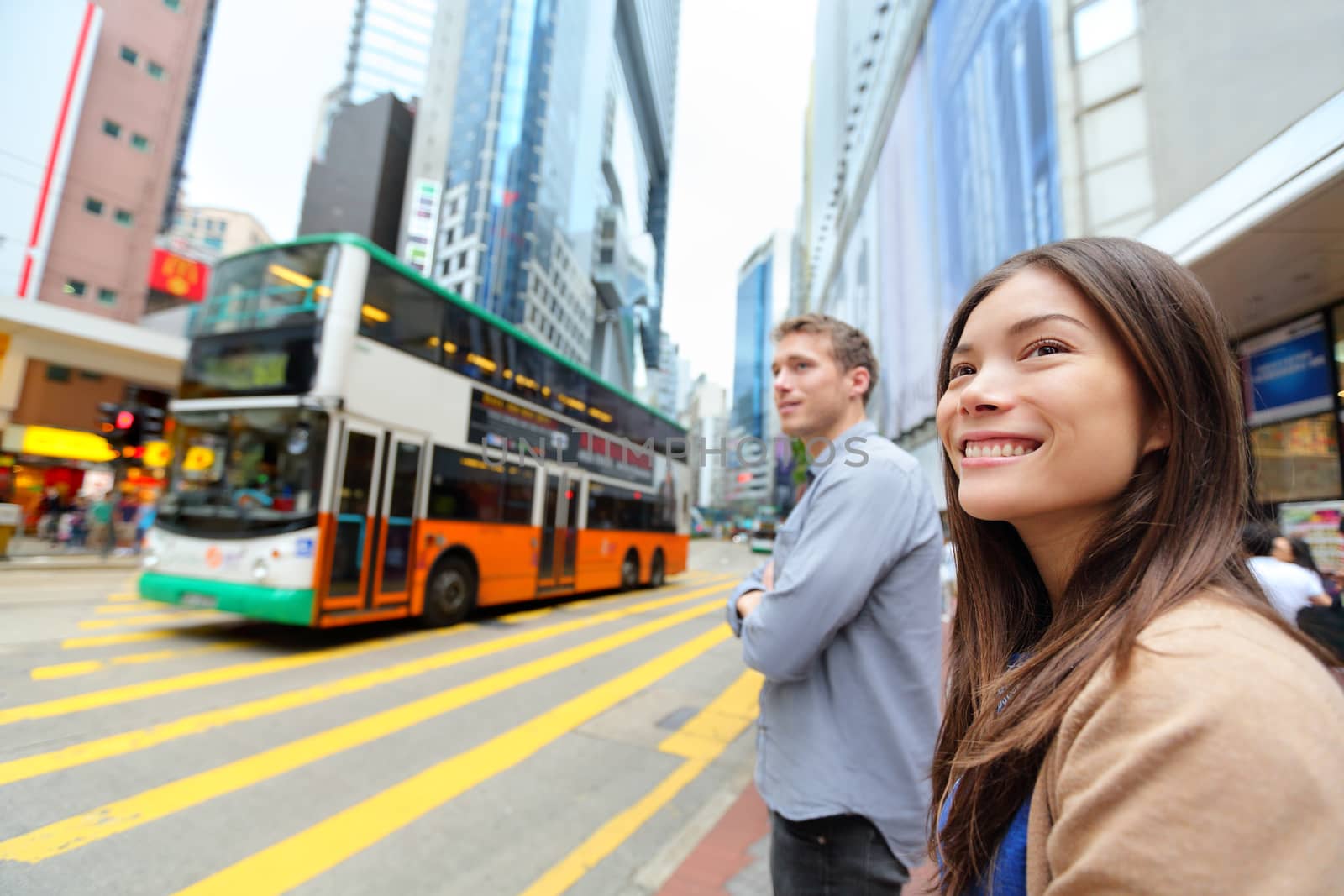 Hong Kong People walking in Causeway Bay crossing busy road with double decker bus. Urban mixed race Asian Chinese / Caucasian woman smiling happy living in city.