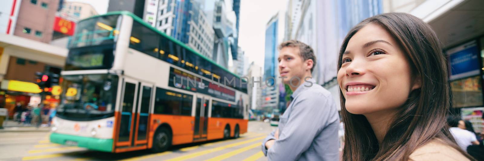 City people lifestyle banner of couple walking crossing the street with double decker bus driving down the road background. Panoramic landscape banner crop. Happy Asian woman, Caucasian man.