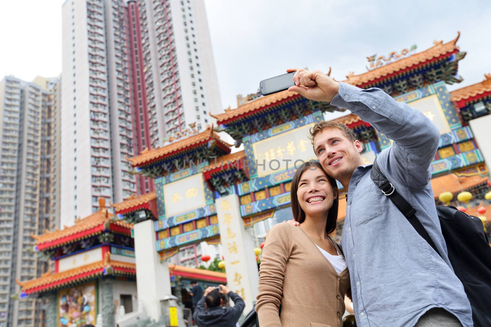 Hong Kong tourist attraction Wong Tai Sin Temple. Tourists taking selfie photo pictures by famous Hong Kong landmark. Romantic couple visiting and sightseeing Taoist temple. Asian woman, Caucasian man