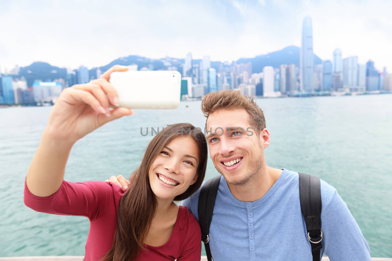 Selfie - friends taking self-portrait picture photo in Hong Kong enjoying sightseeing on Tsim Sha Tsui Promenade and Avenue of Stars in Victoria Harbour, Kowloon, Hong Kong. Travel concept.