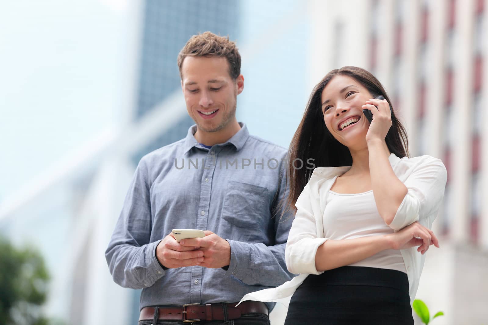 Young urban professionals business people on smartphones in Hong Kong. Businessman using app on smartphone and businesswoman talking having conversation on smart phone in Hong Kong Central.