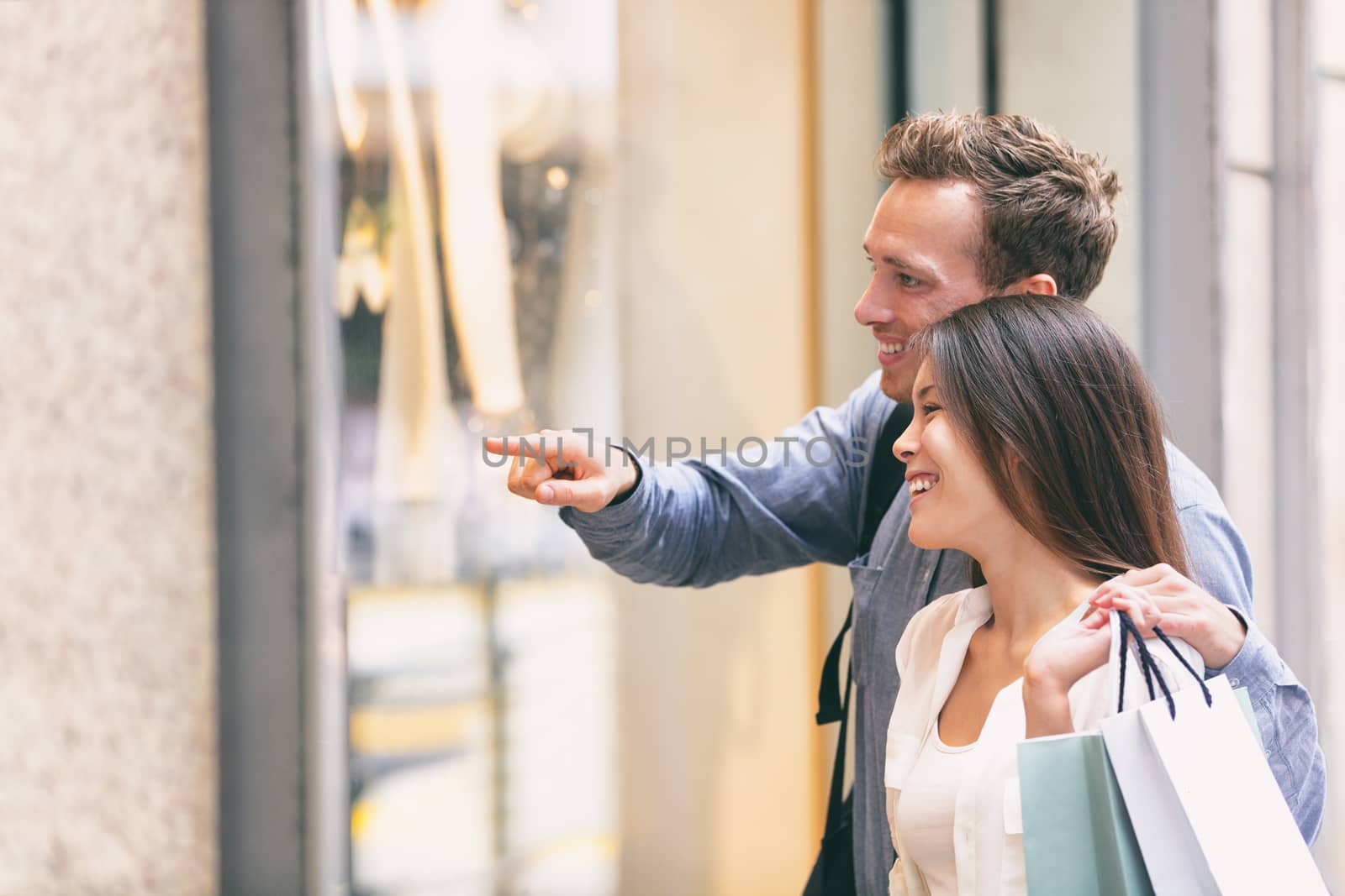 Couple shopping looking at shop window holding shopping bags. Multiracial Asian Chinese woman shopper and Caucasian man smiling happy walking in the street living in city. People city lifestyle.