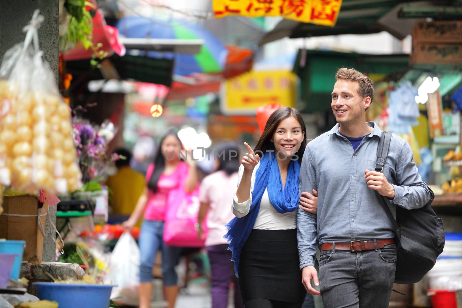 Young couple tourists walking shopping in street food market in Hong Kong. Couple looking around at stand shops. Asian woman, Caucasian man interracial people. by Maridav