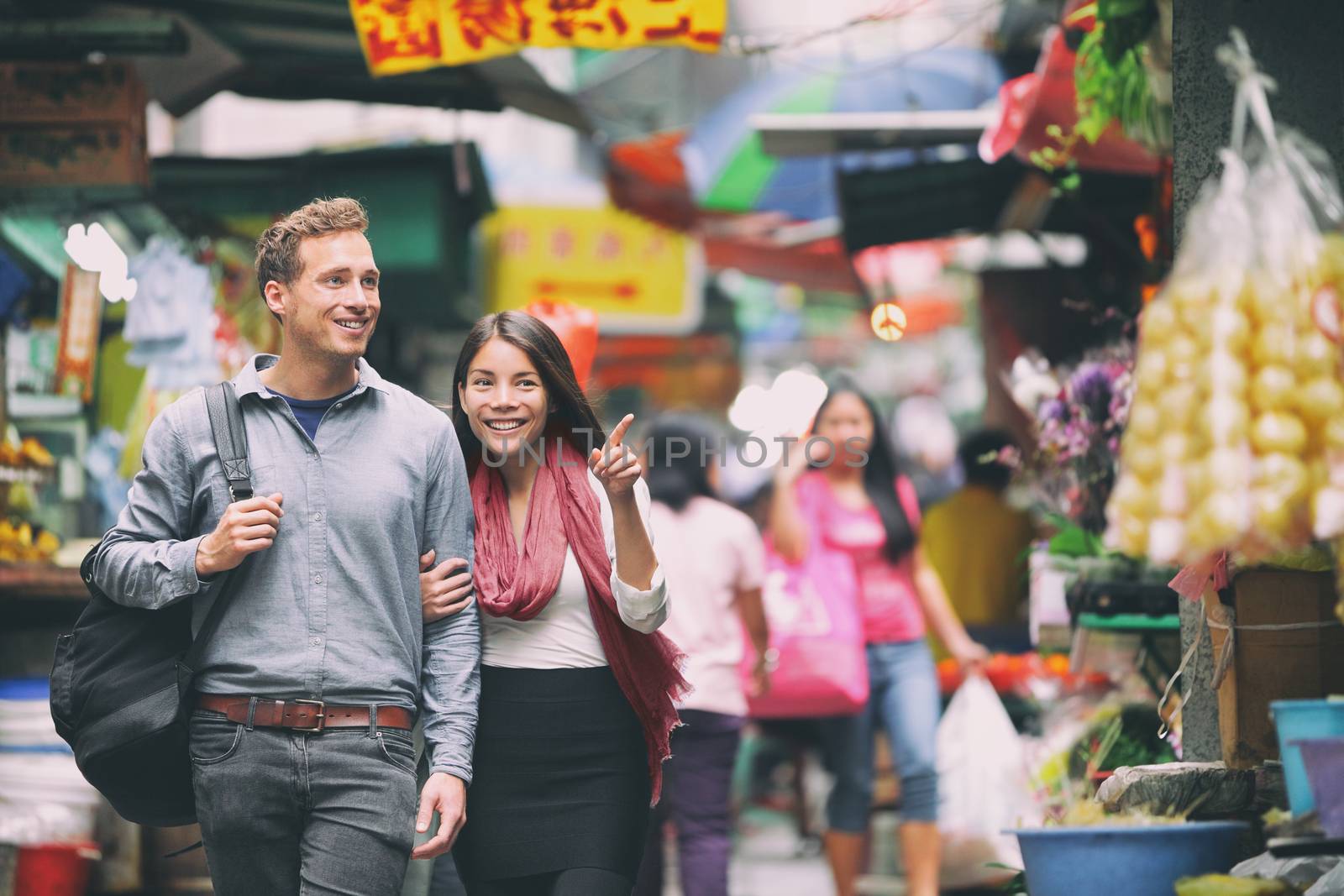 Interracial couple tourists walking shopping in chinese market in Hong Kong, China. Young people traveling in Asia looking at local street food. Asian woman, Caucasian man. by Maridav