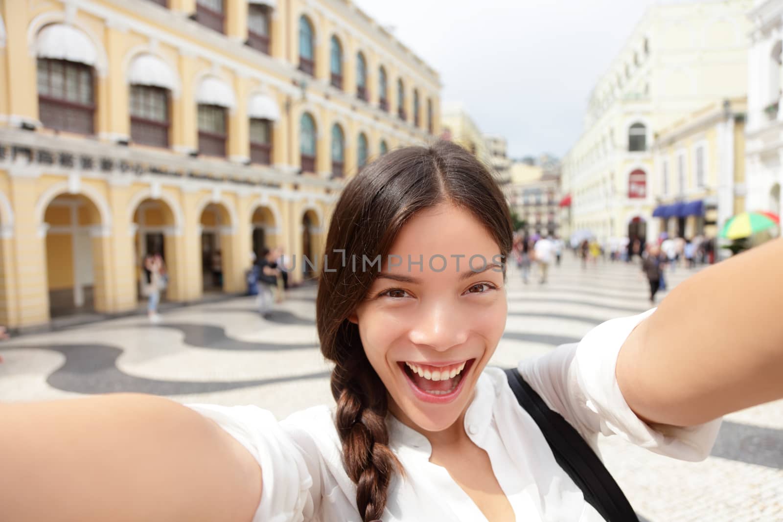 Selfie woman taking fun selfportrait in Macau, China in Senado Square or Senate Square. Asian girl tourist using smart phone camera to take photo while traveling in Macau. Travel and tourism concept.