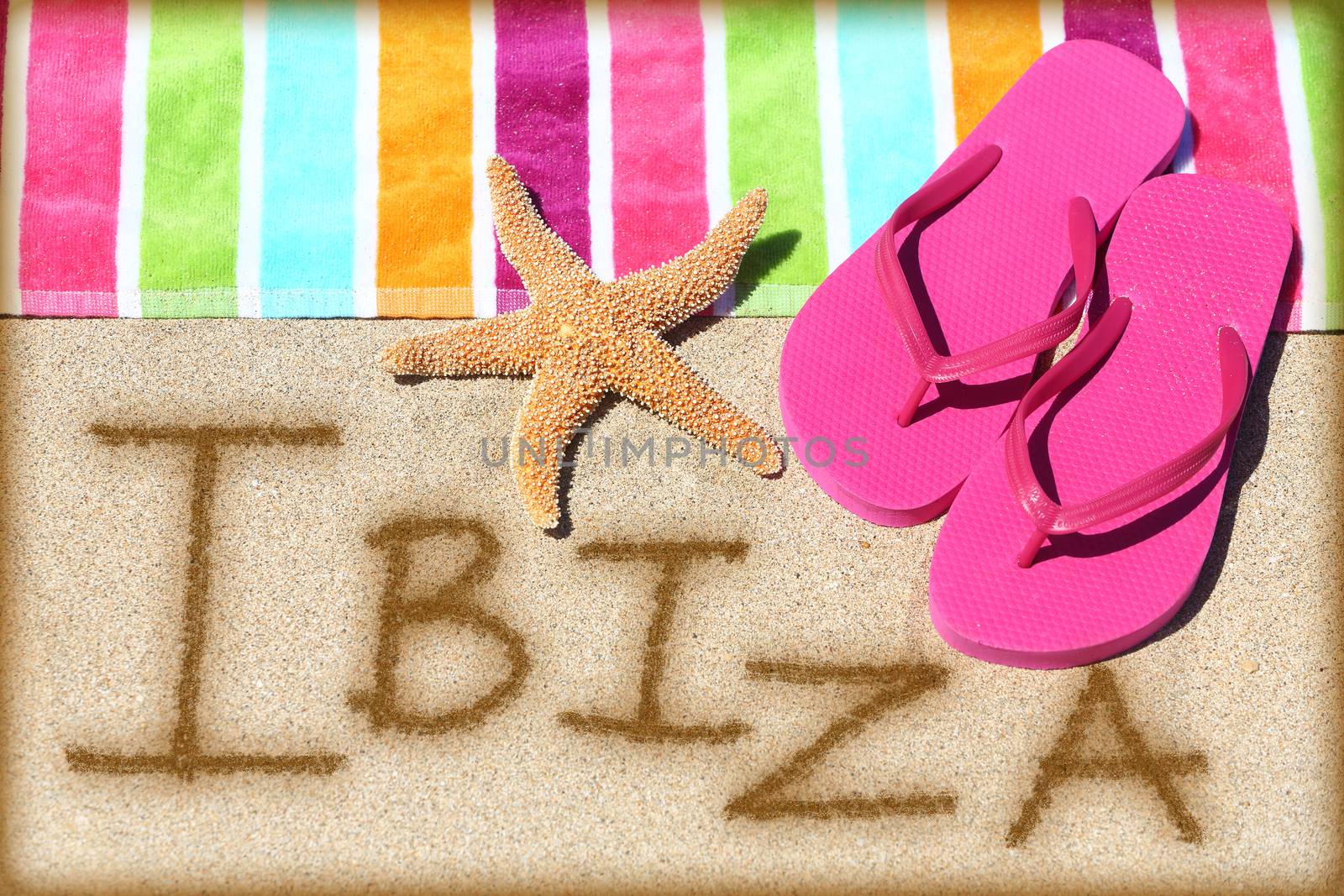 Ibiza beach travel concept background. IBIZA written in sand with water next to beach towel, summer sandals and starfish. Summer and sun vacation holidays on Balearic Islands, Spain.