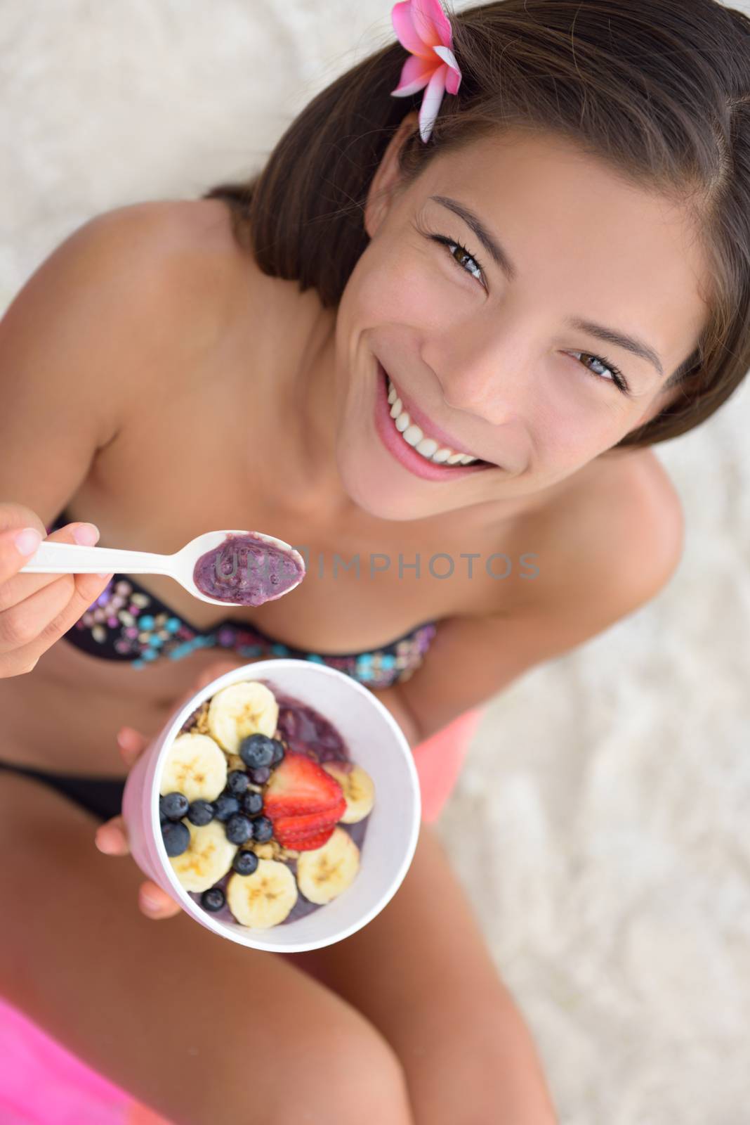 Acai bowl - woman eating healthy food on beach. Girl enjoy acai bowls made from acai berries and fruits outdoors on beach for breakfast. Girl on Hawaii eating local Hawaiian dish.
