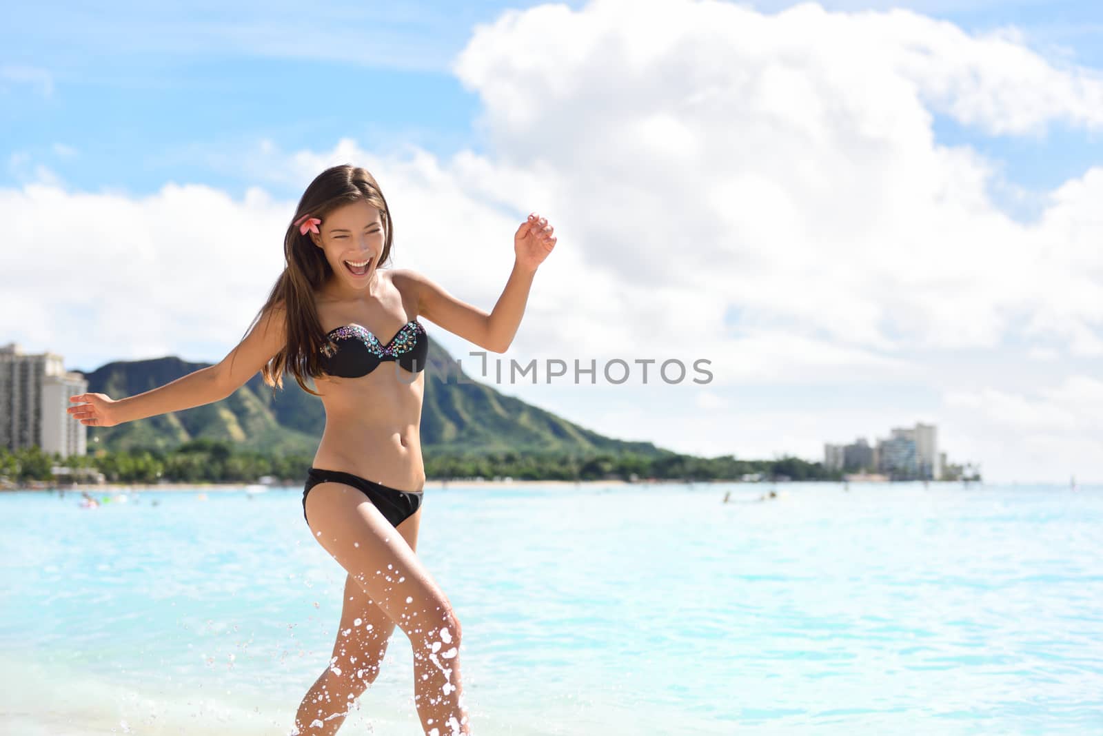 Beach woman in bikini on Waikiki, Oahu, Hawaii, USA. Girl on travel vacation holidays running having fun splashing water on Hawaiian Waikiki beach with Diamond Head mountain. Asian Caucasian model.